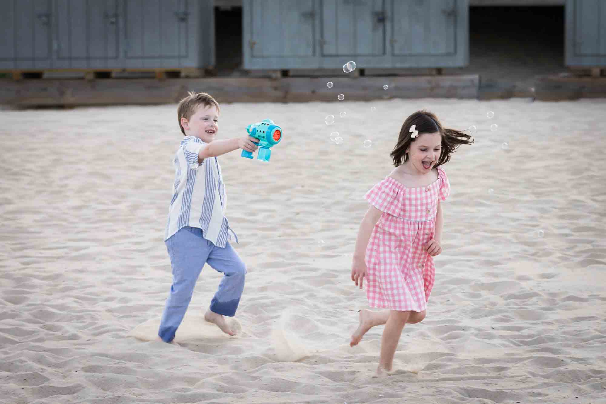 Little boy chasing little girl with bubble gun on the beach for an article on how to get the best beach photos