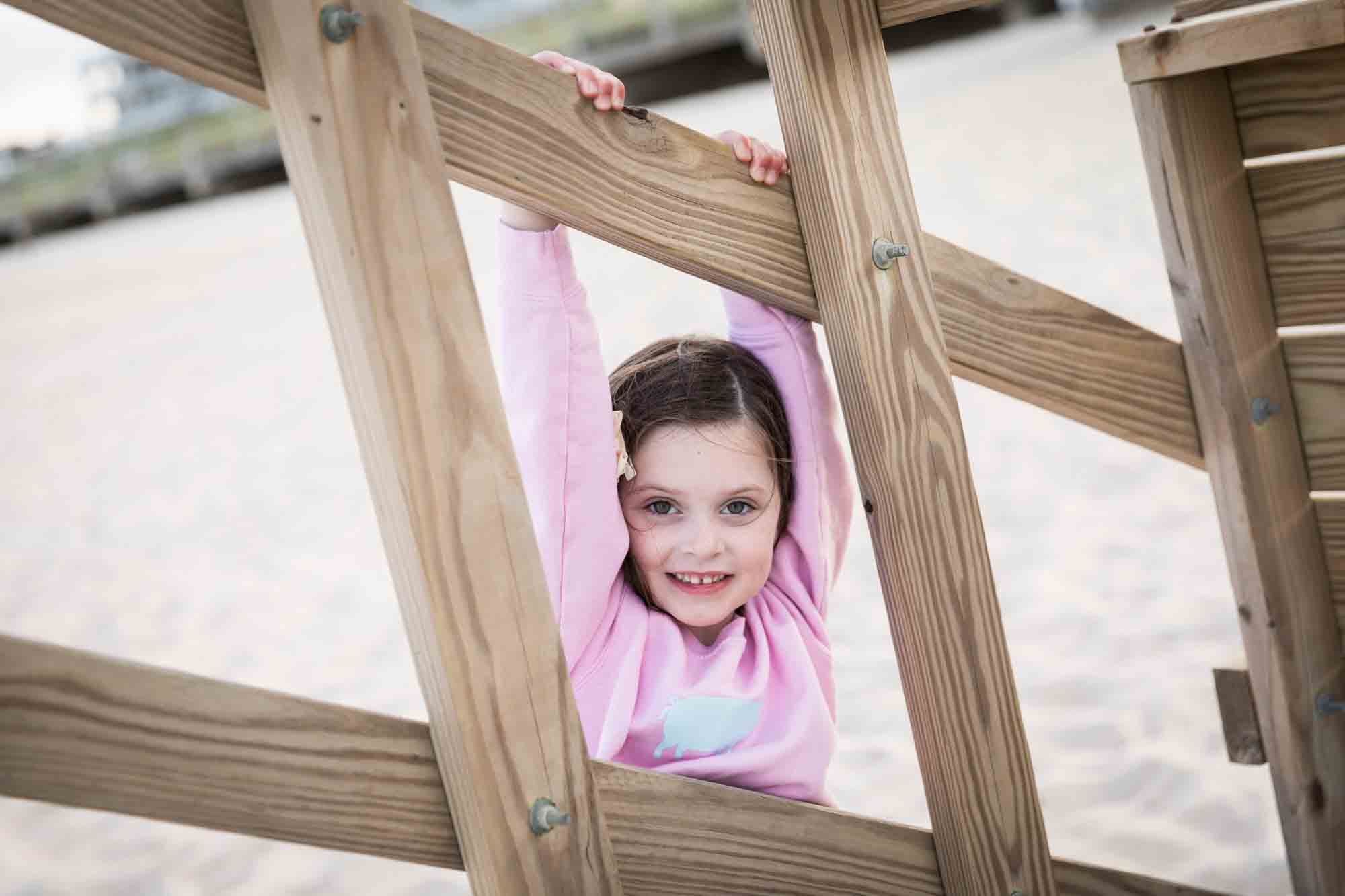 Little girl in pink shirt hanging from wooden rafter