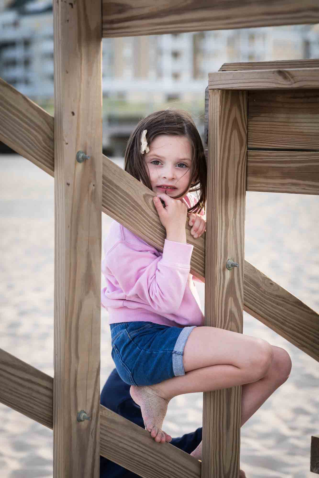 Little girl in pink shirt hanging from wooden rafter