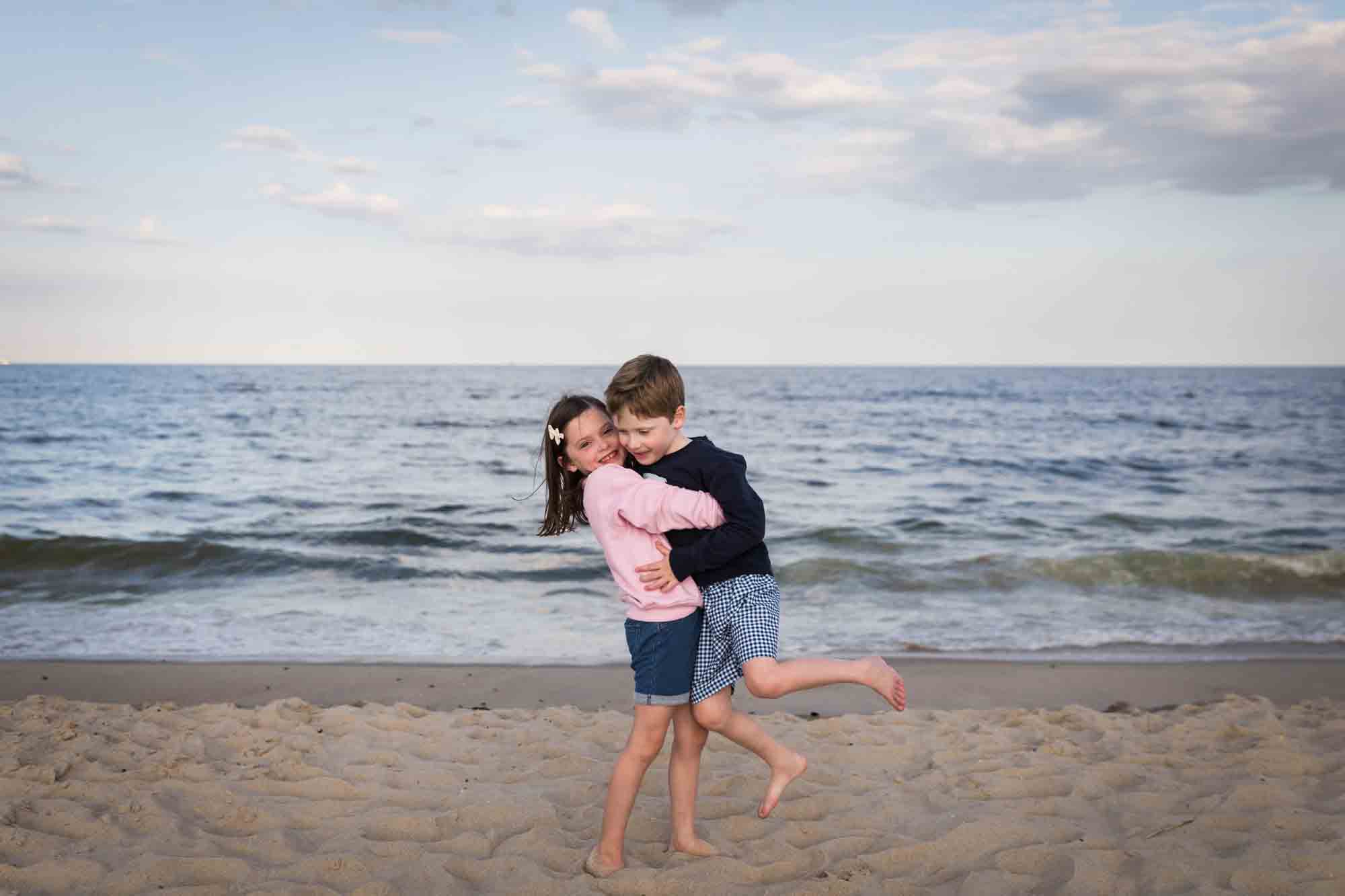 Little girl lifting up little boy on beach in front of ocean