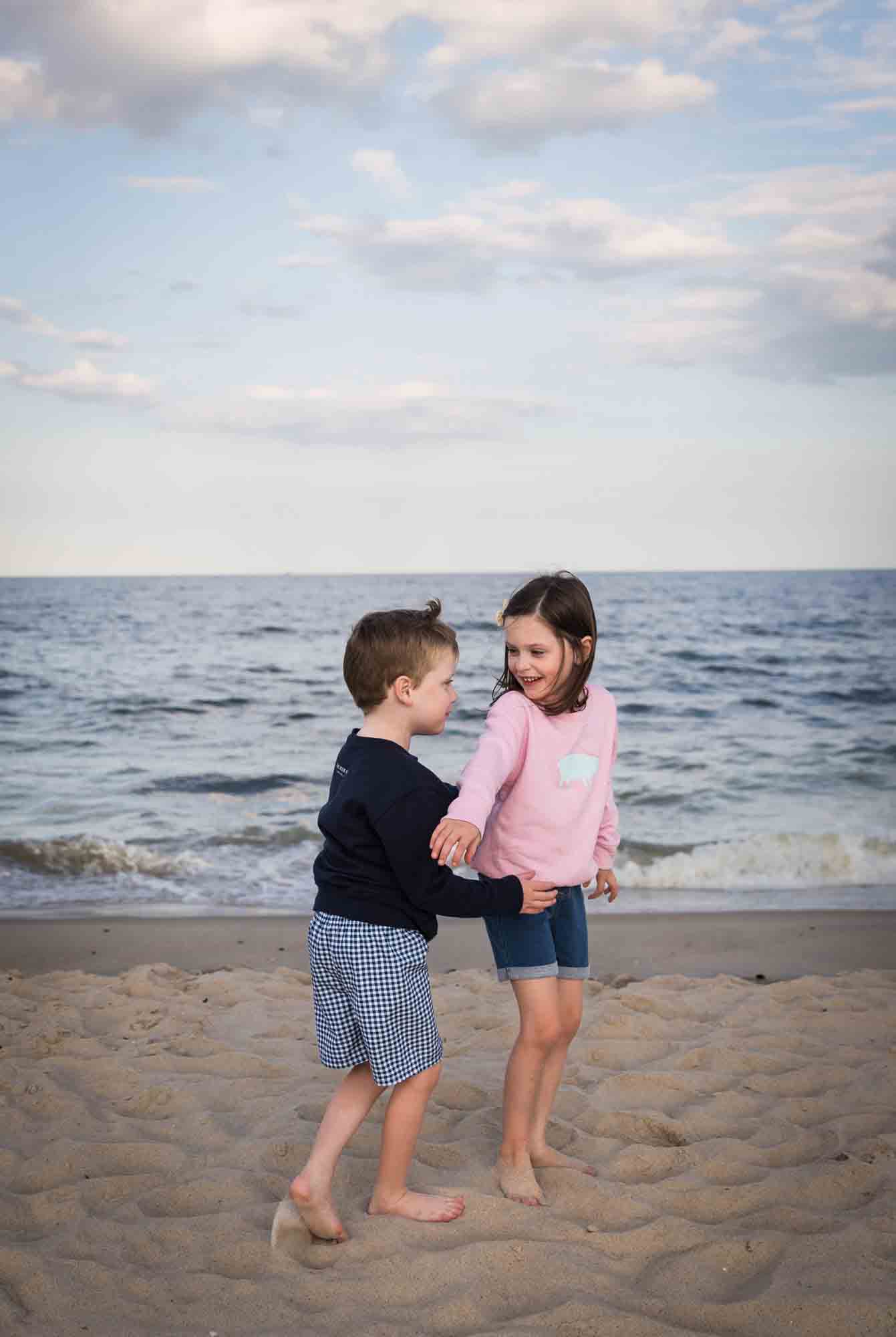 Little boy lifting up little girl on beach in front of ocean