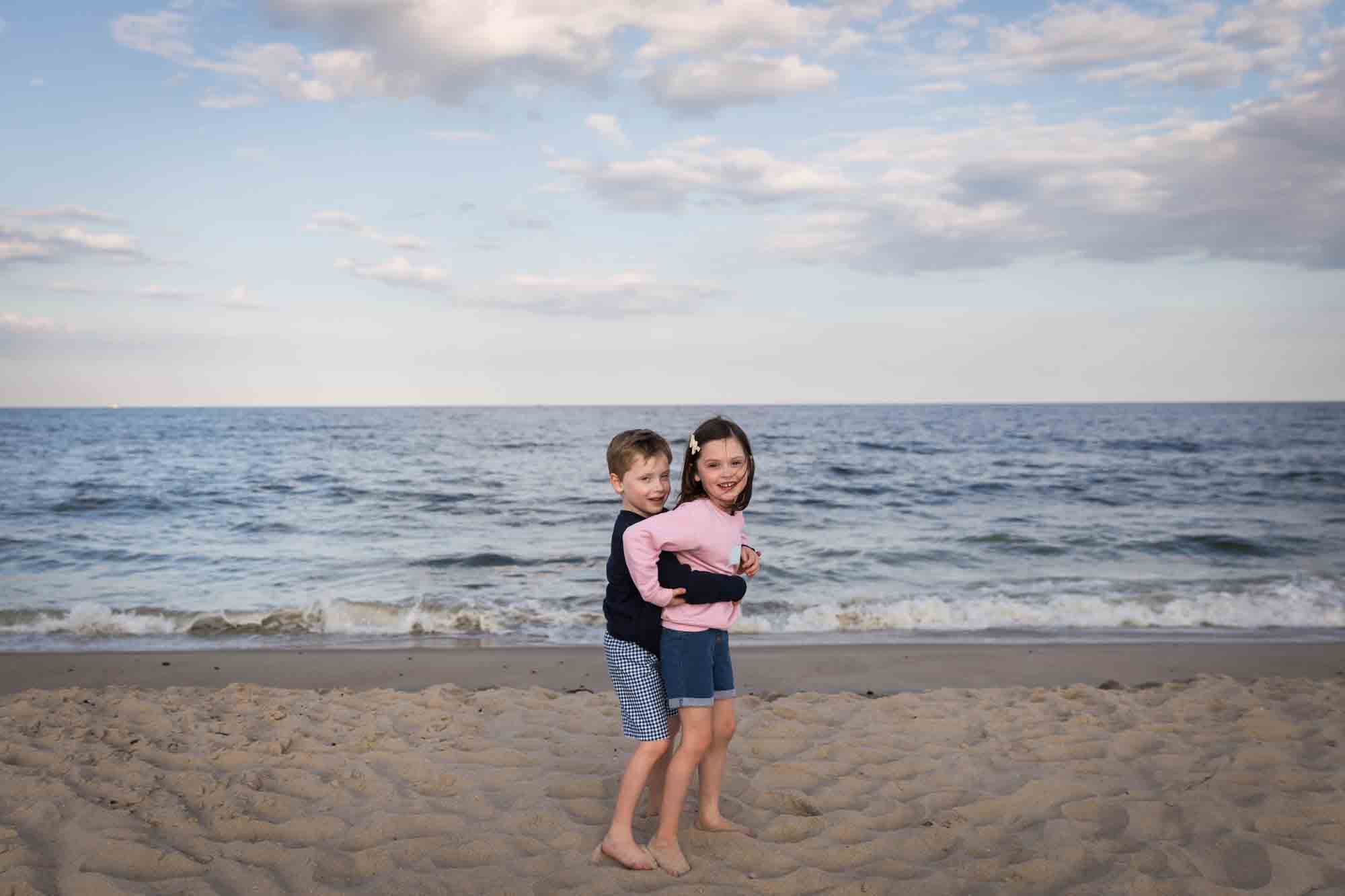 Little boy lifting up little girl on beach in front of ocean