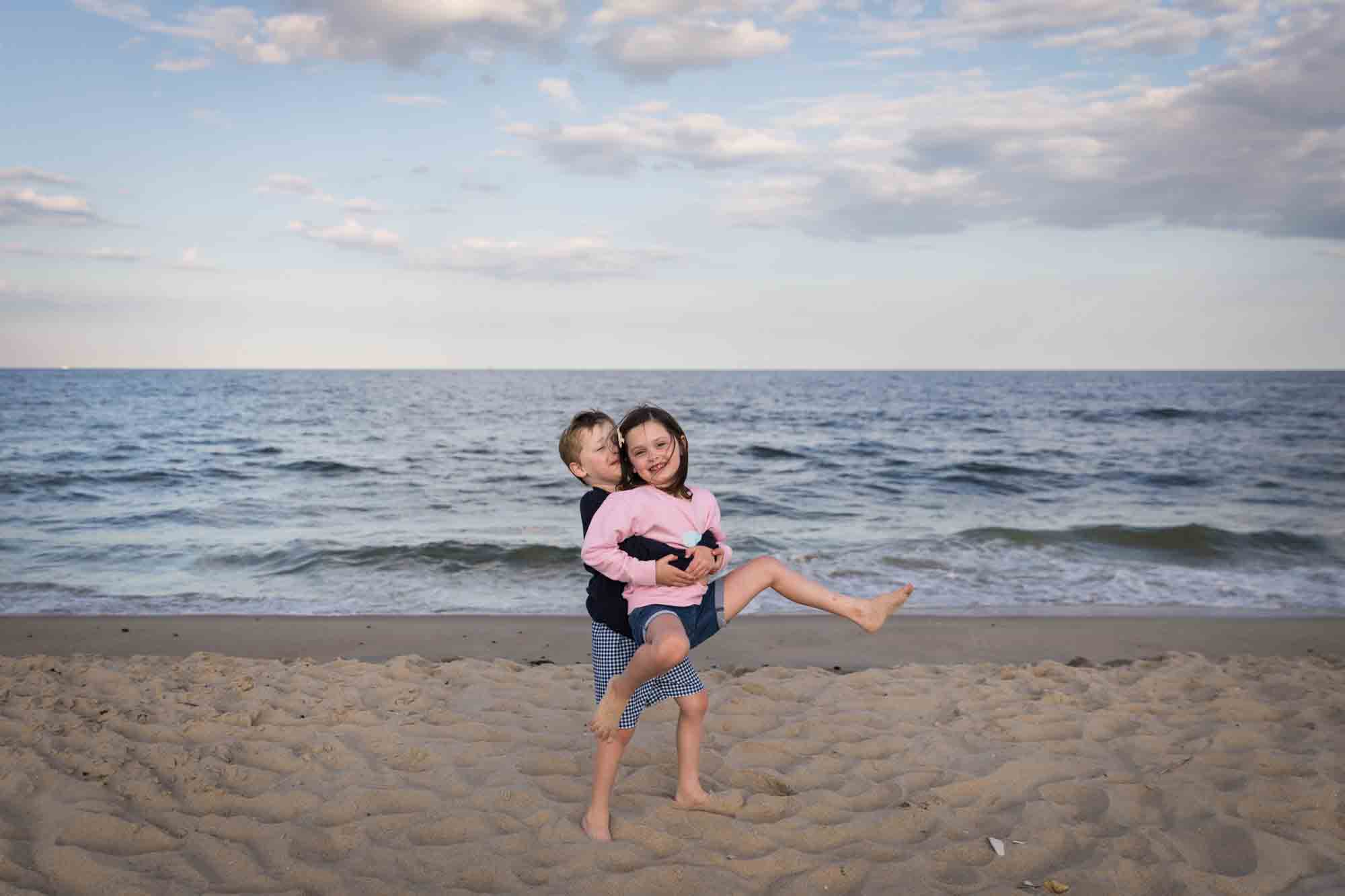 Little boy lifting up little girl on beach in front of ocean