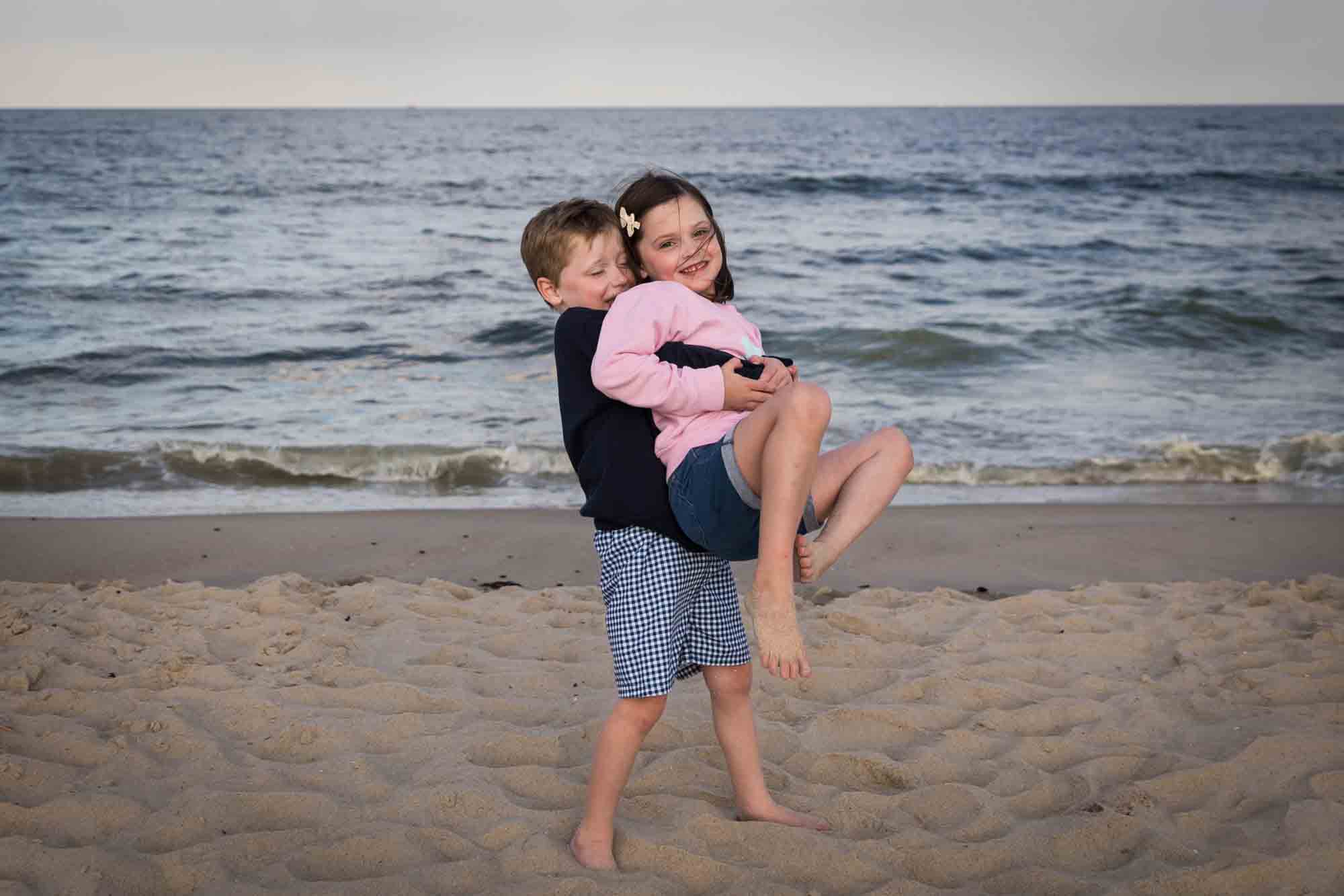 Little boy lifting up little girl on beach in front of ocean