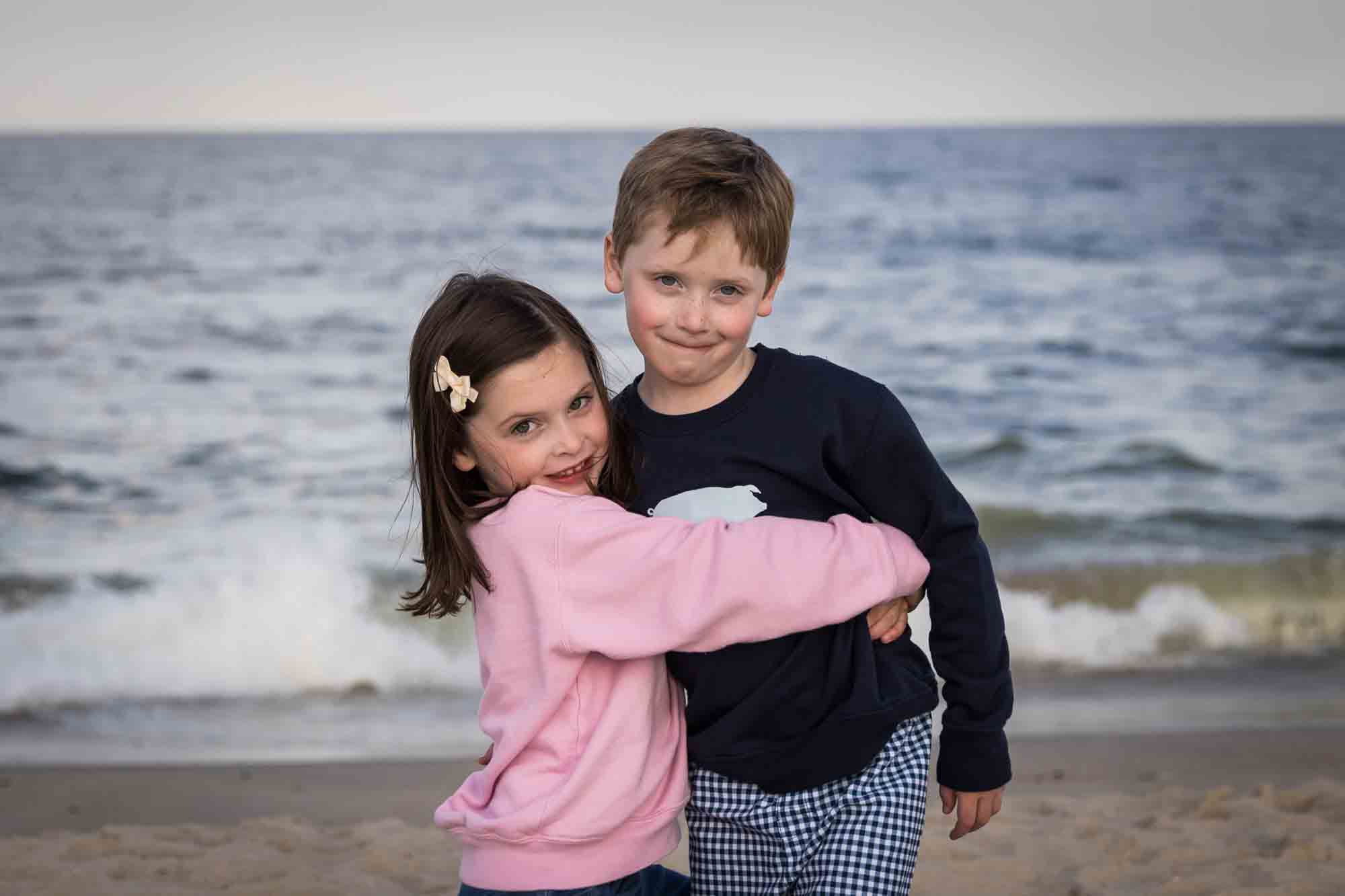 Little girl lifting up little boy on beach in front of ocean