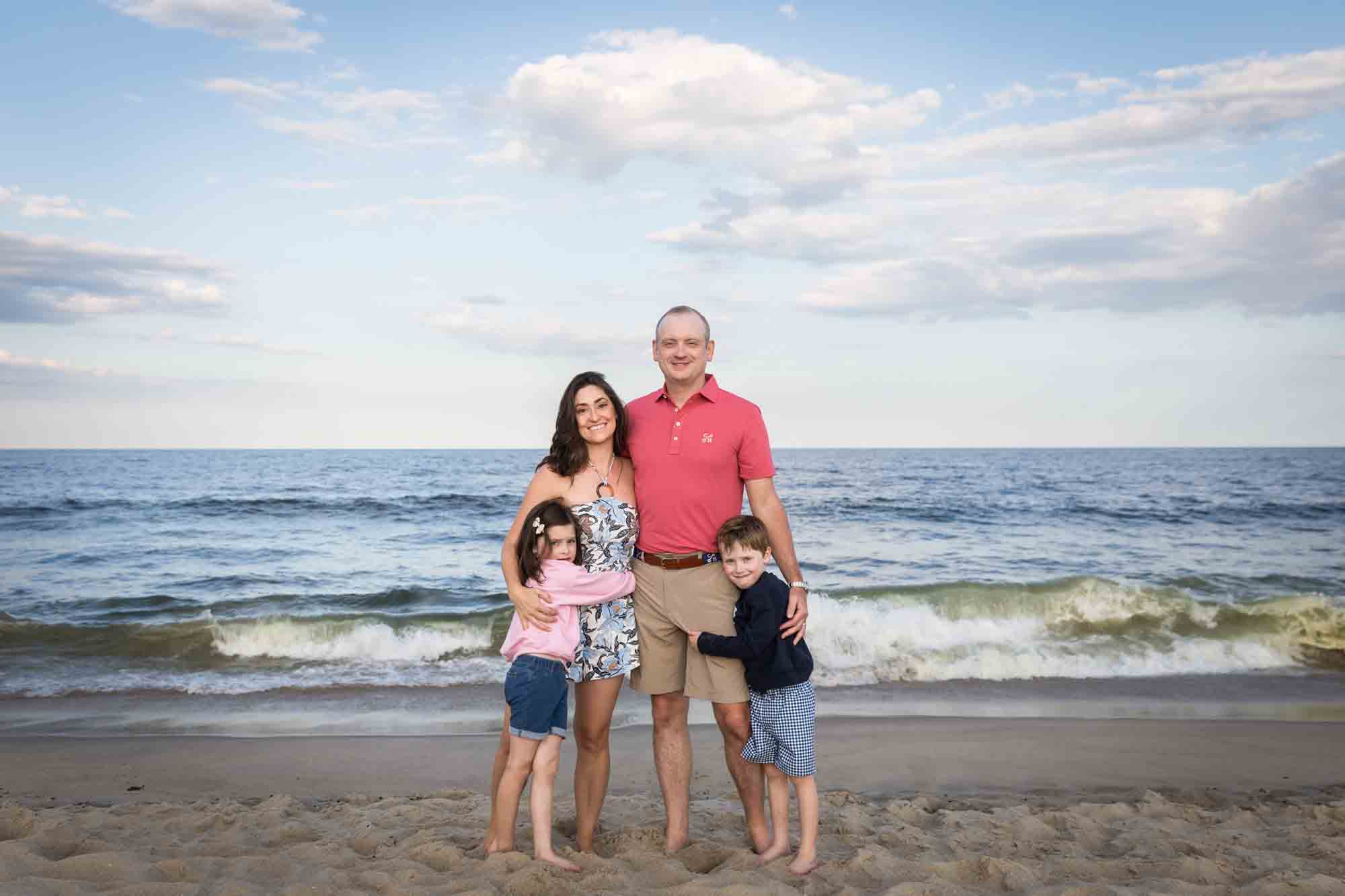 Parents and two kids standing on beach in front of sky and ocean for an article on how to get the best beach photos