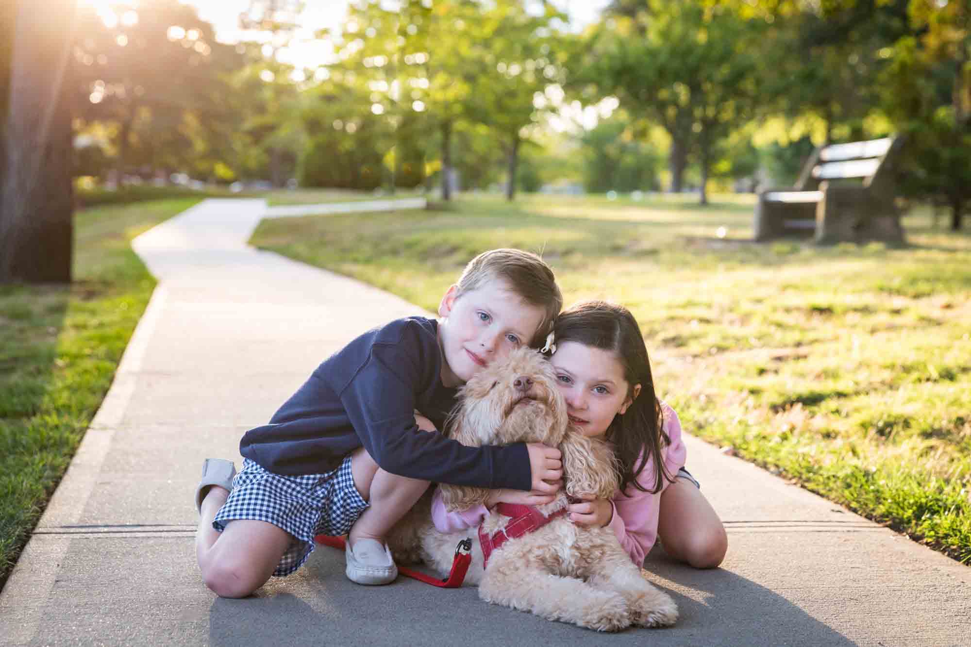 Little boy and girl giving hug to dog on the sidewalk at sunset