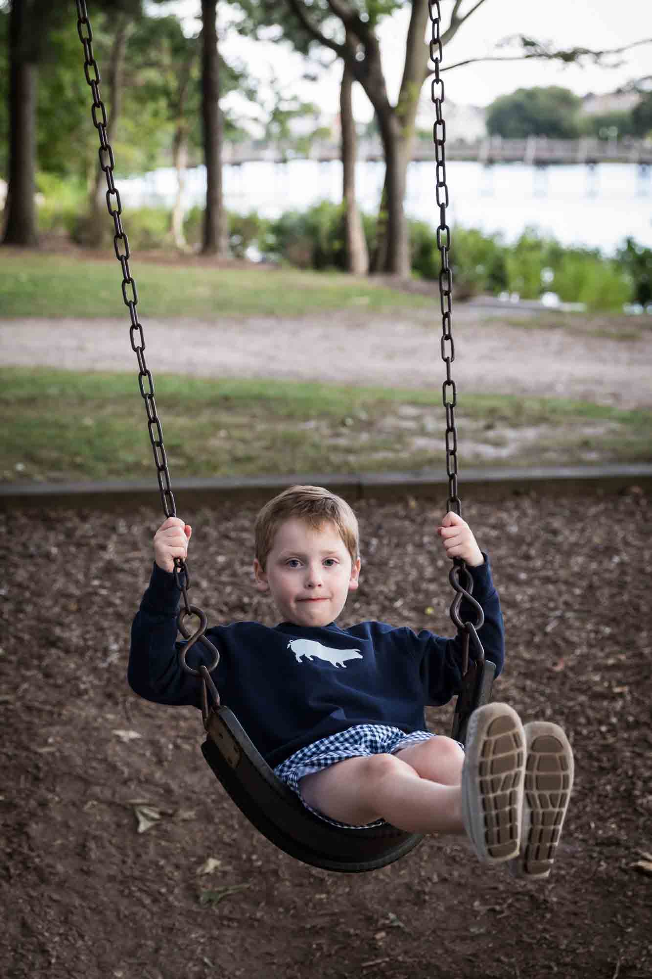 Little boy in blue sweatshirt swinging in swings at playground