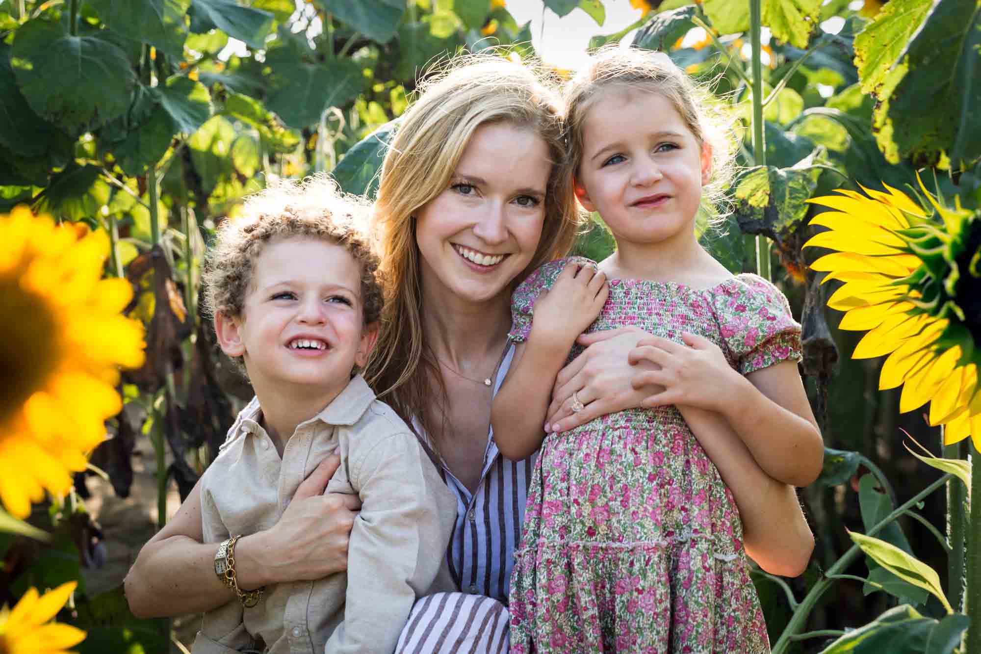 Mother hugging two small children in sunflower patch