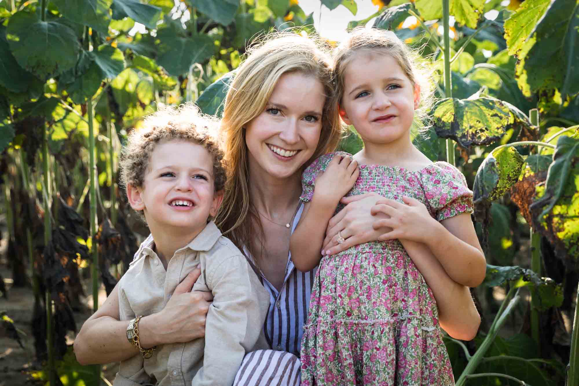 Mother hugging two small children in sunflower patch