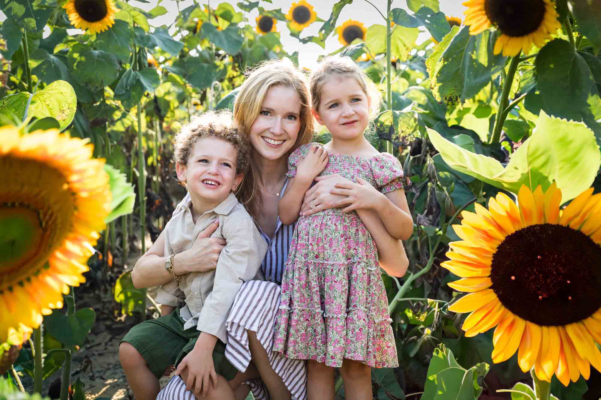 Mother hugging two small children in sunflower patch