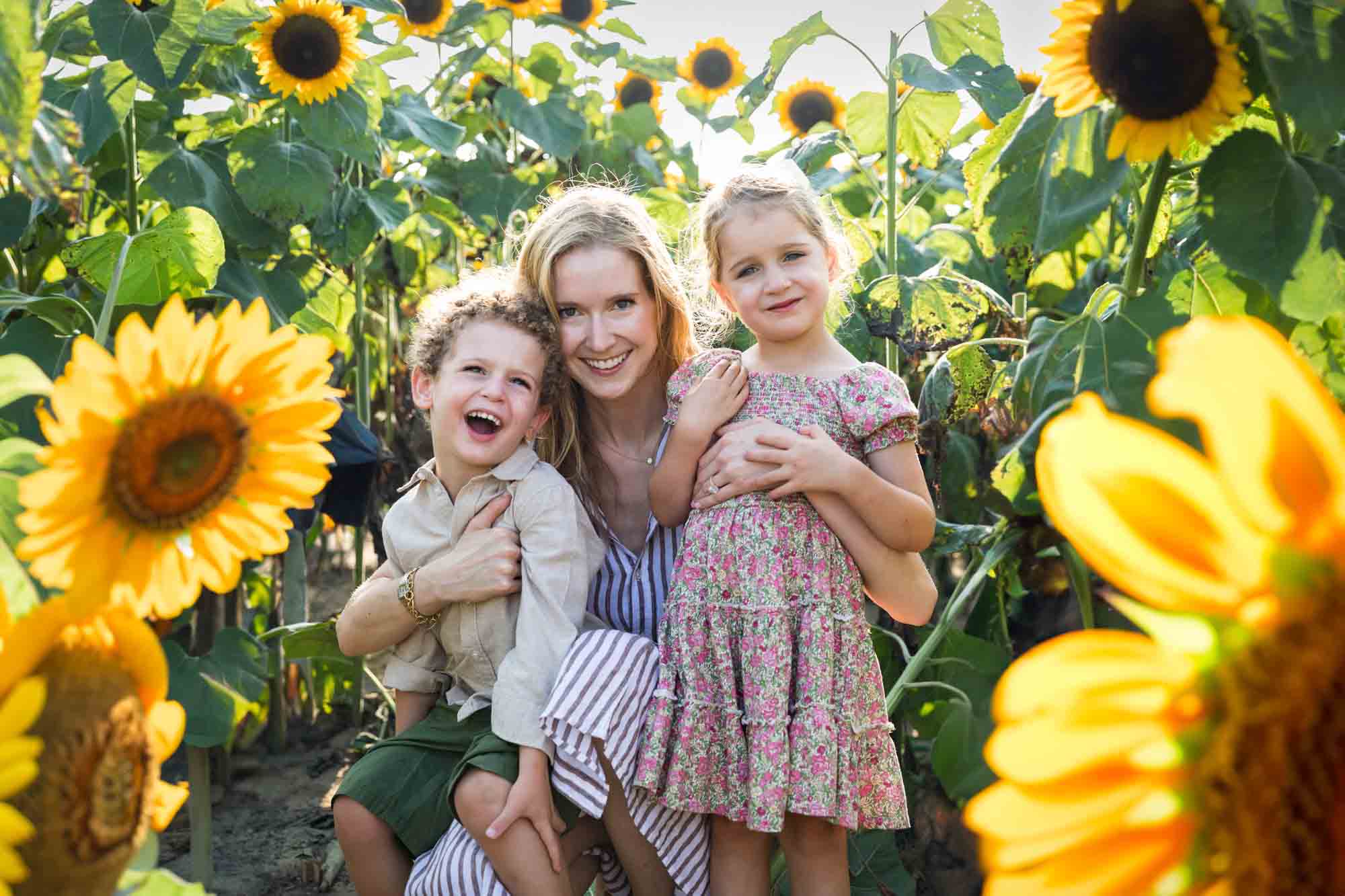 Mother hugging two small children in sunflower patch