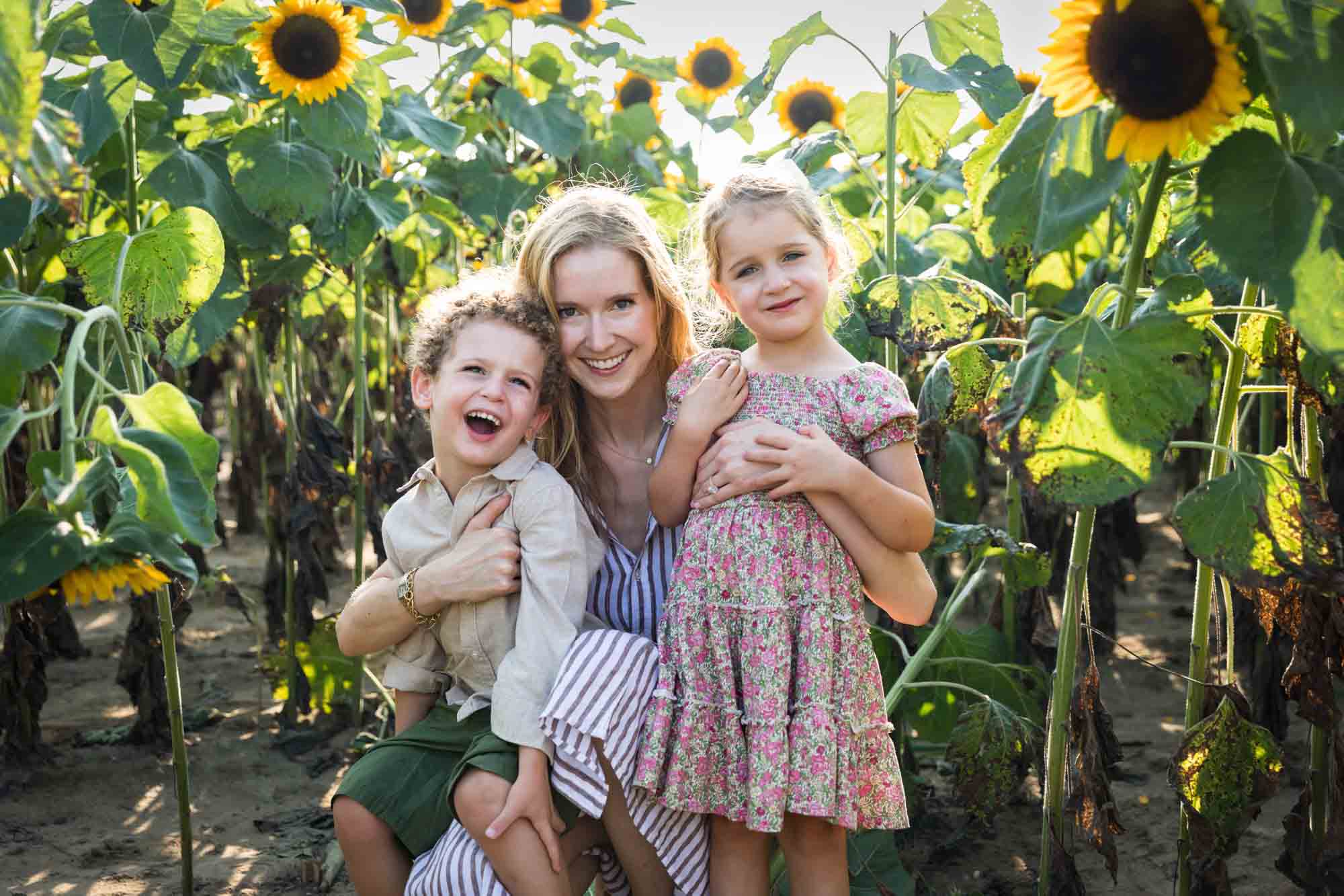 Mother hugging two small children in sunflower patch