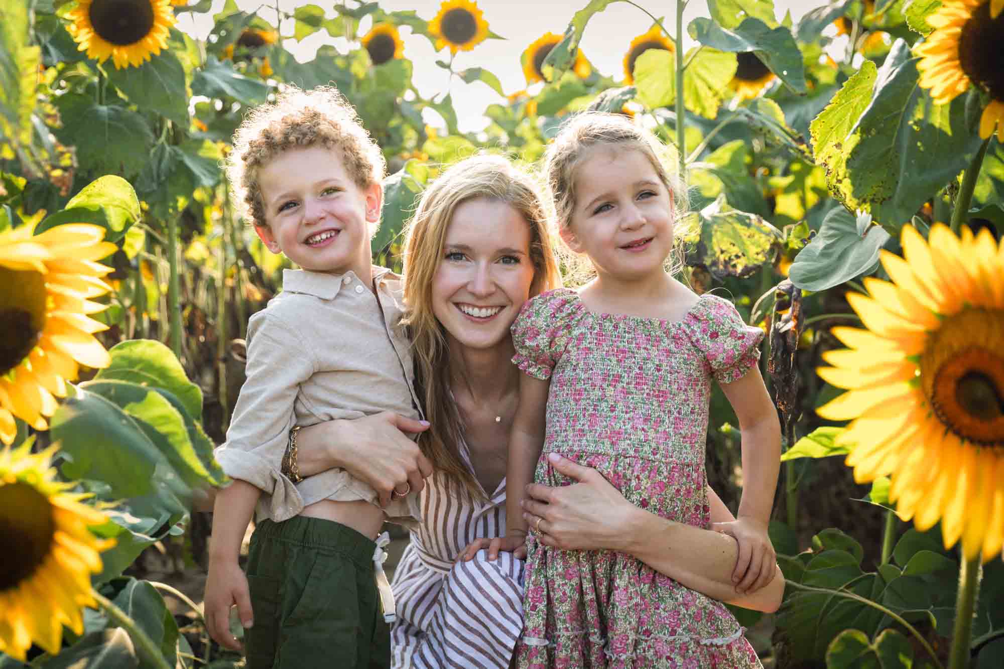 Mother hugging two small children in sunflower patch