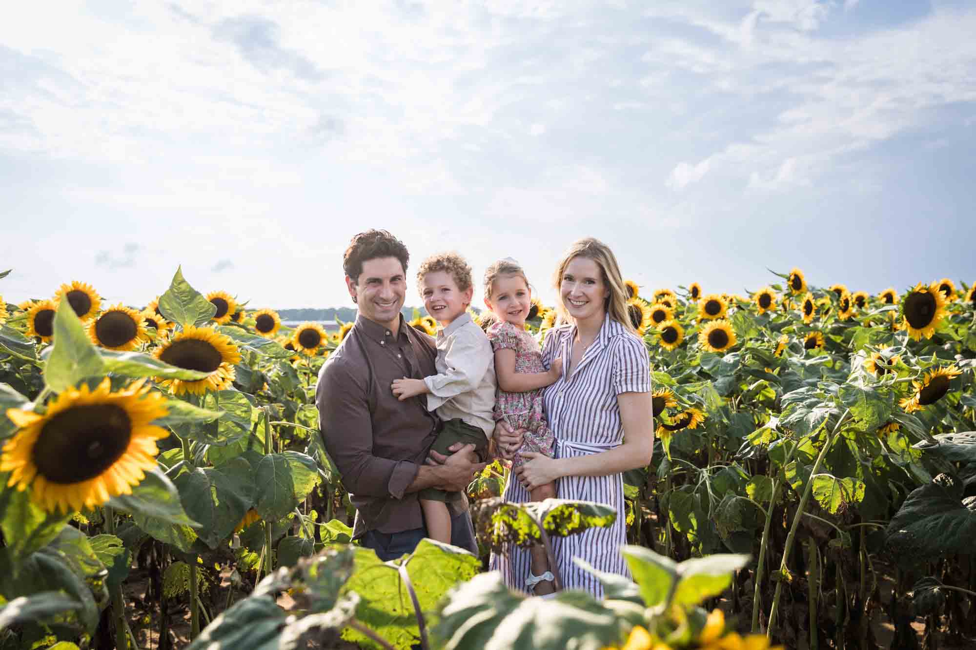 Parents holding two small children in sunflower patch 