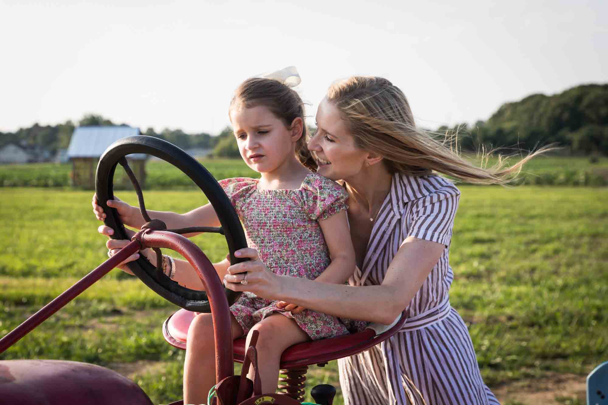 Mother helping little girl drive tractor