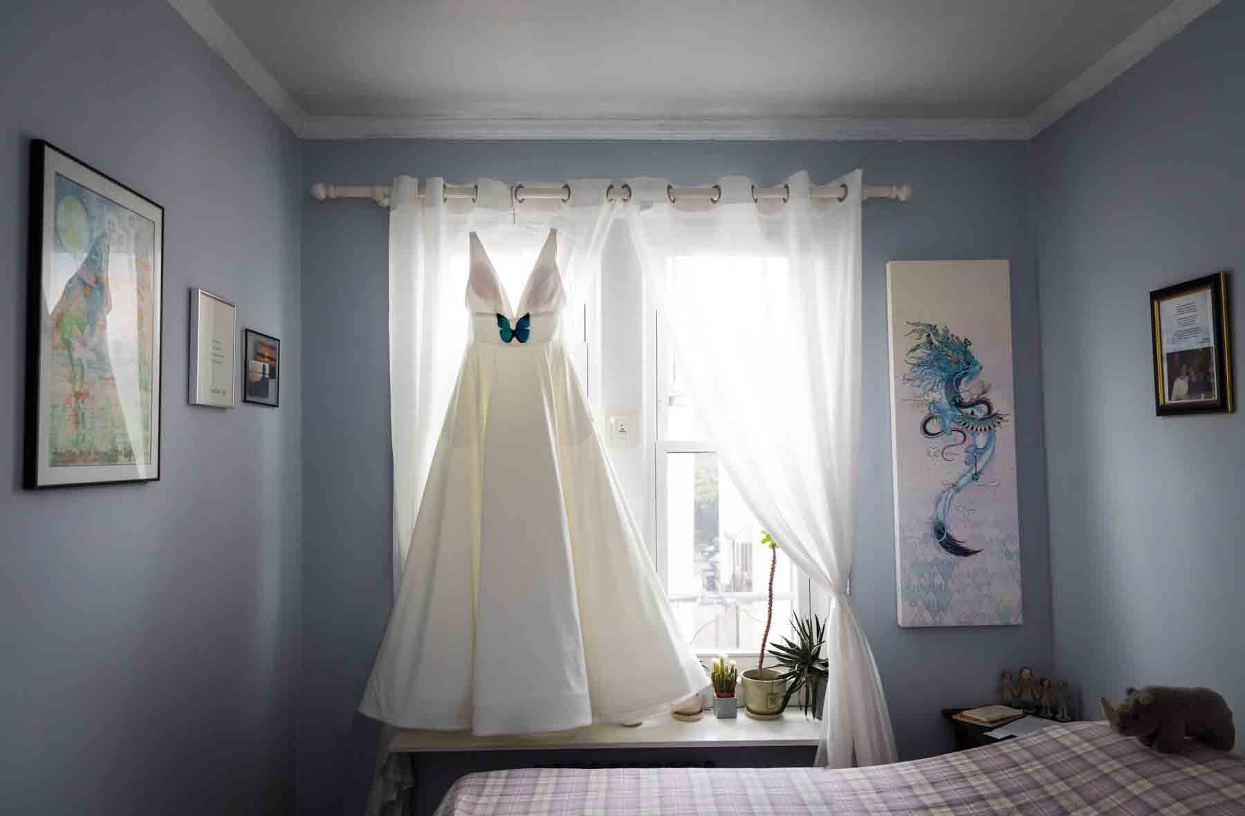 Wedding dress with butterfly hanging on curtain rod in bedroom