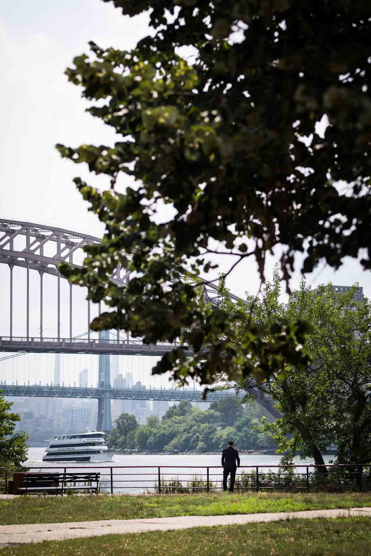 Groom standing along waterfront before first look in Astoria Park