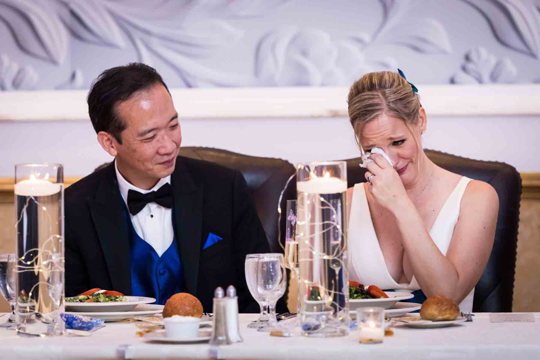 Bride wiping away tears beside groom at a table at a Terrace on the Park wedding
