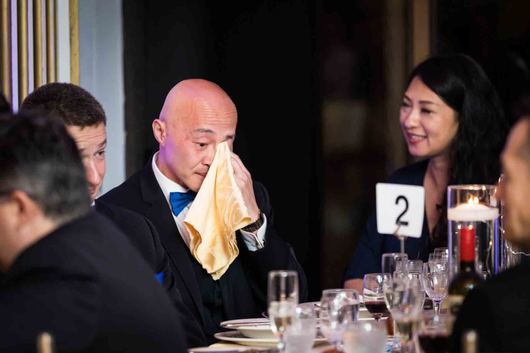 Bald Asian man using yellow napkin to wipe tears at a Terrace on the Park wedding