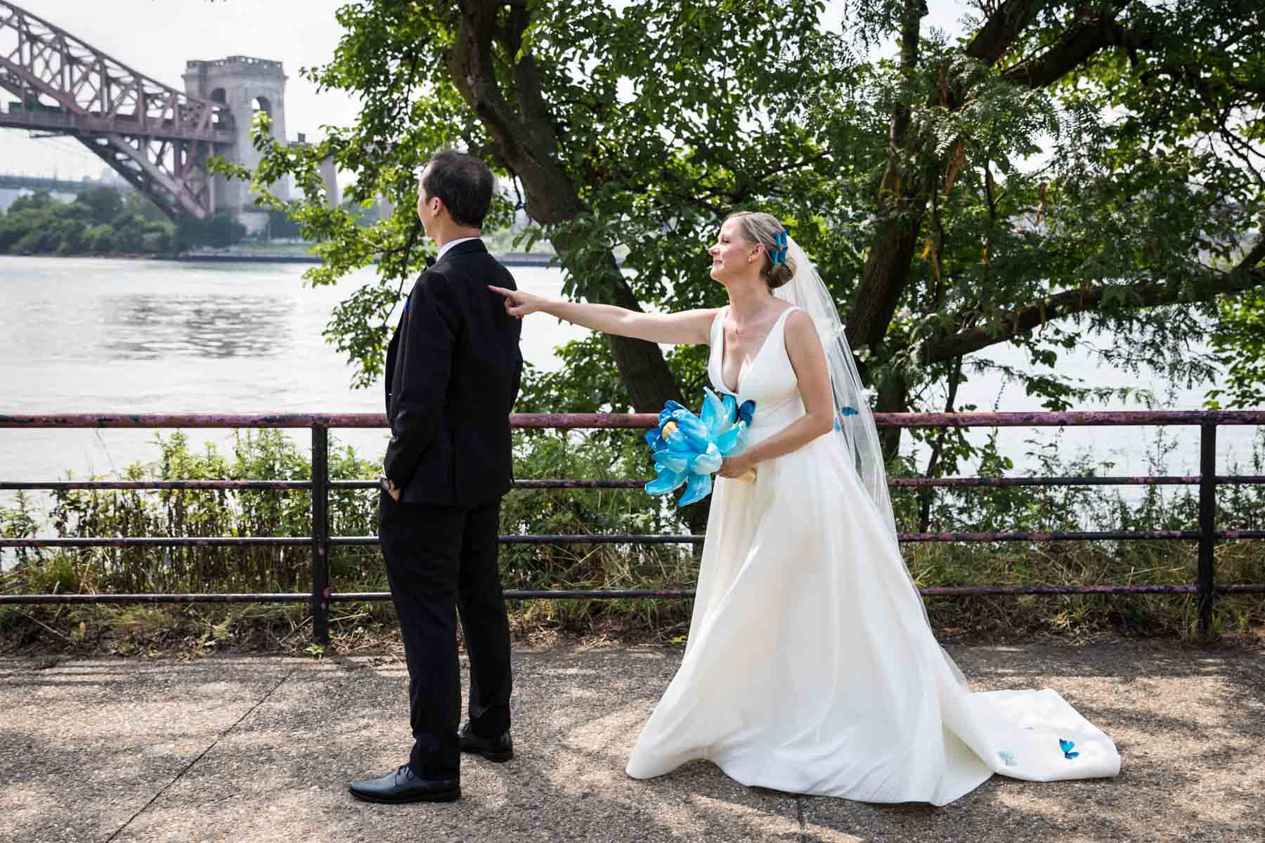 Bride tapping groom on shoulder during first look along waterfront in Astoria Park