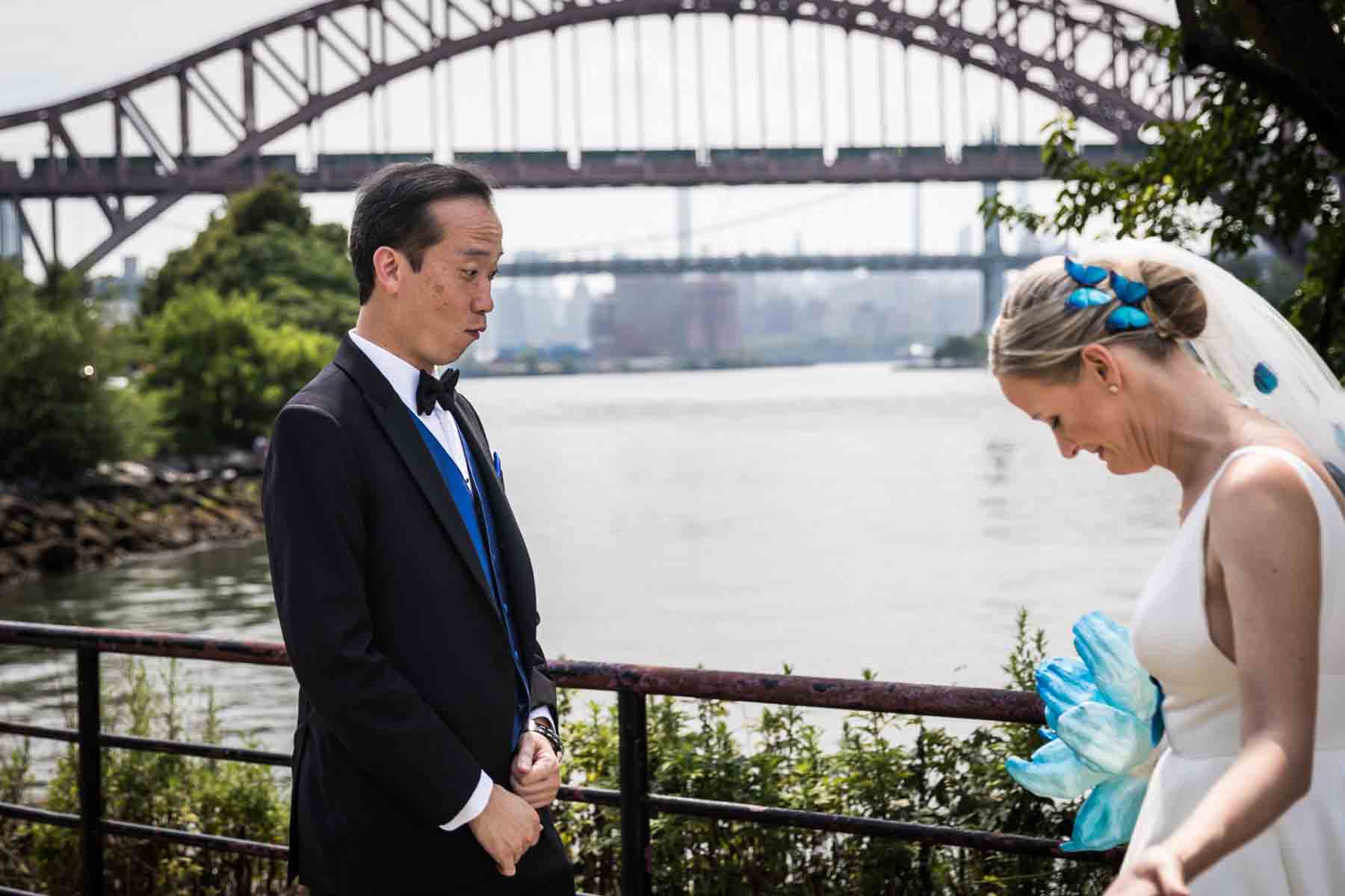 Groom looking at bride in dress during first look along waterfront in Astoria Park