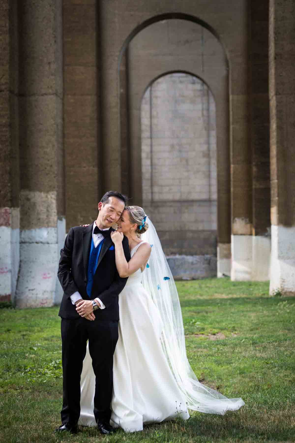 Bride and groom hugging under Hell Gate Bridge arches in Astoria Park