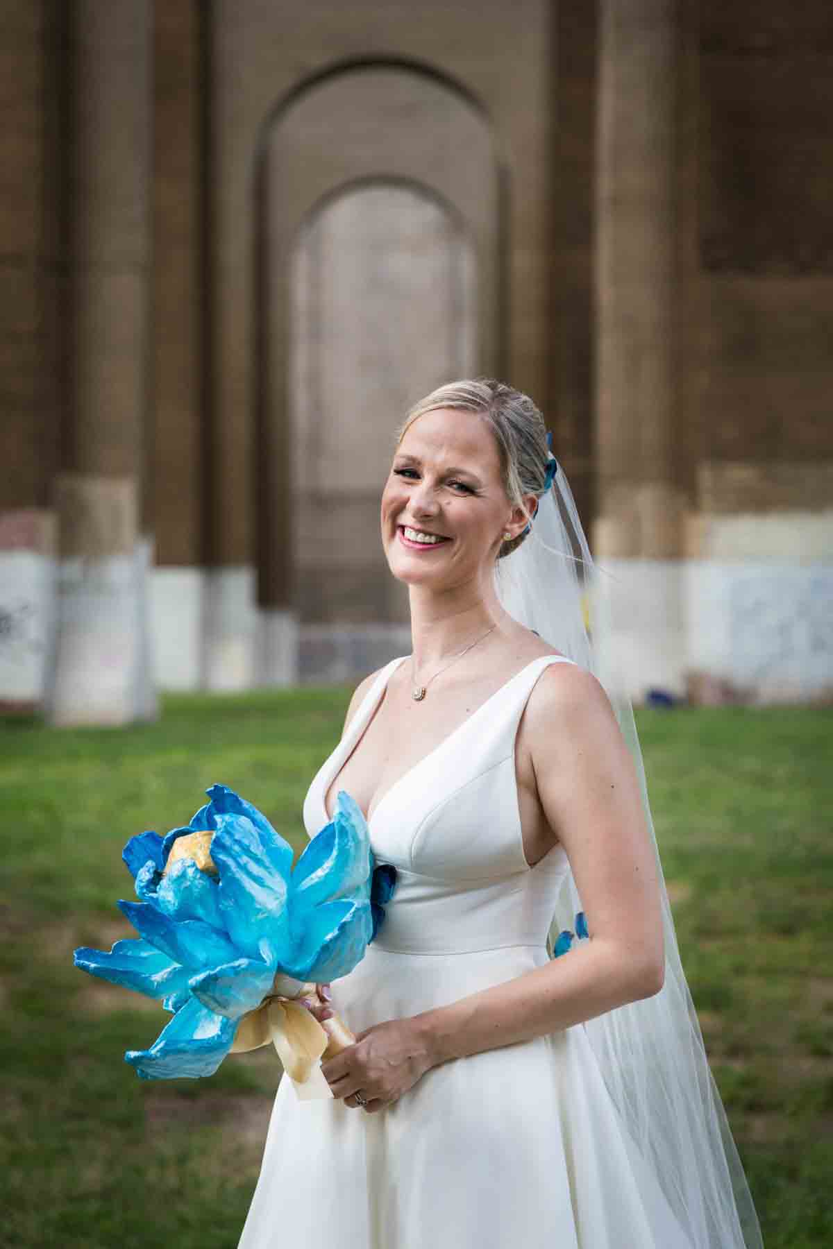 Bride holding blue flower bouquet under Hell Gate Bridge