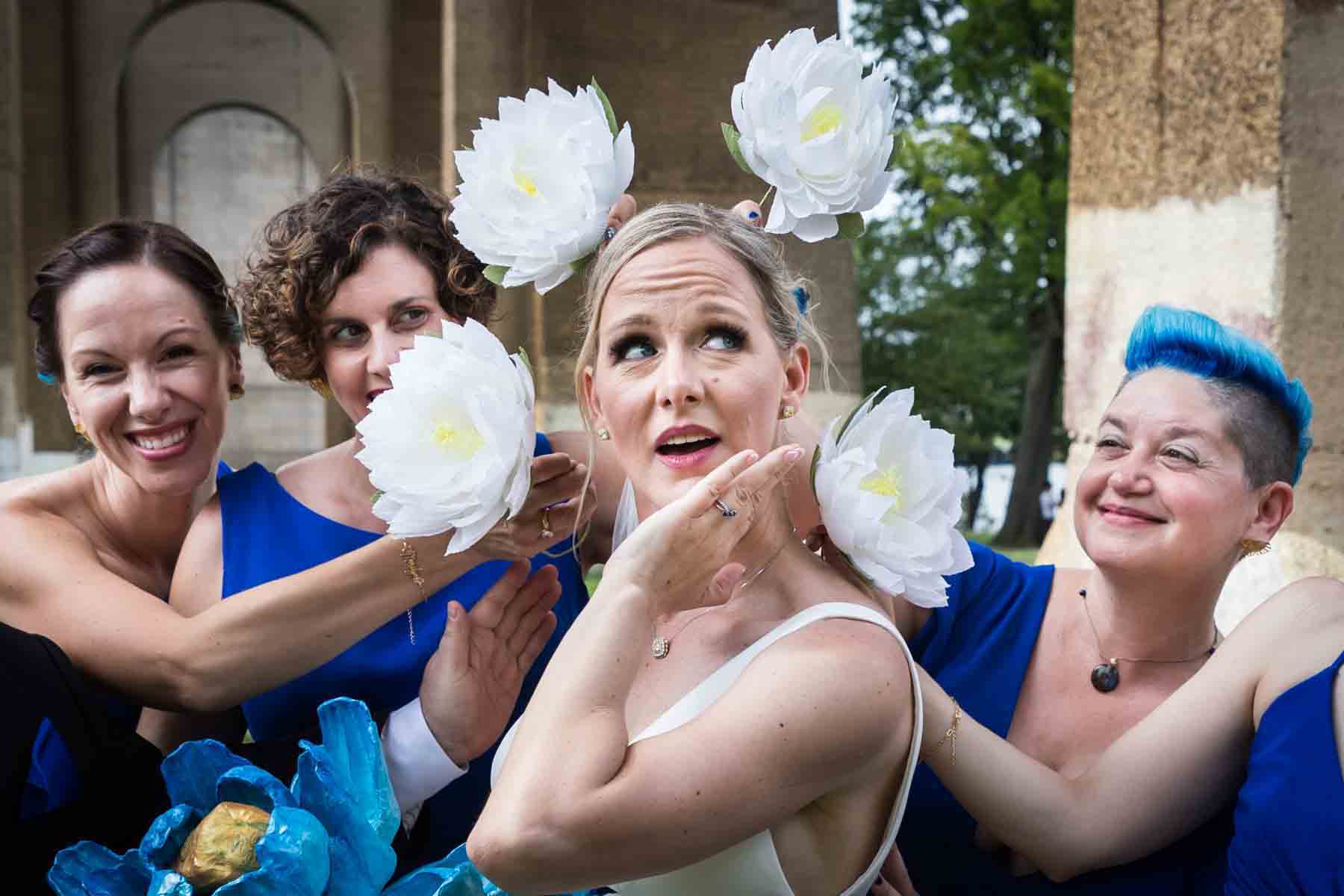 Bride standing under Hell Gate Bridge with bridesmaids holding flowers around her head