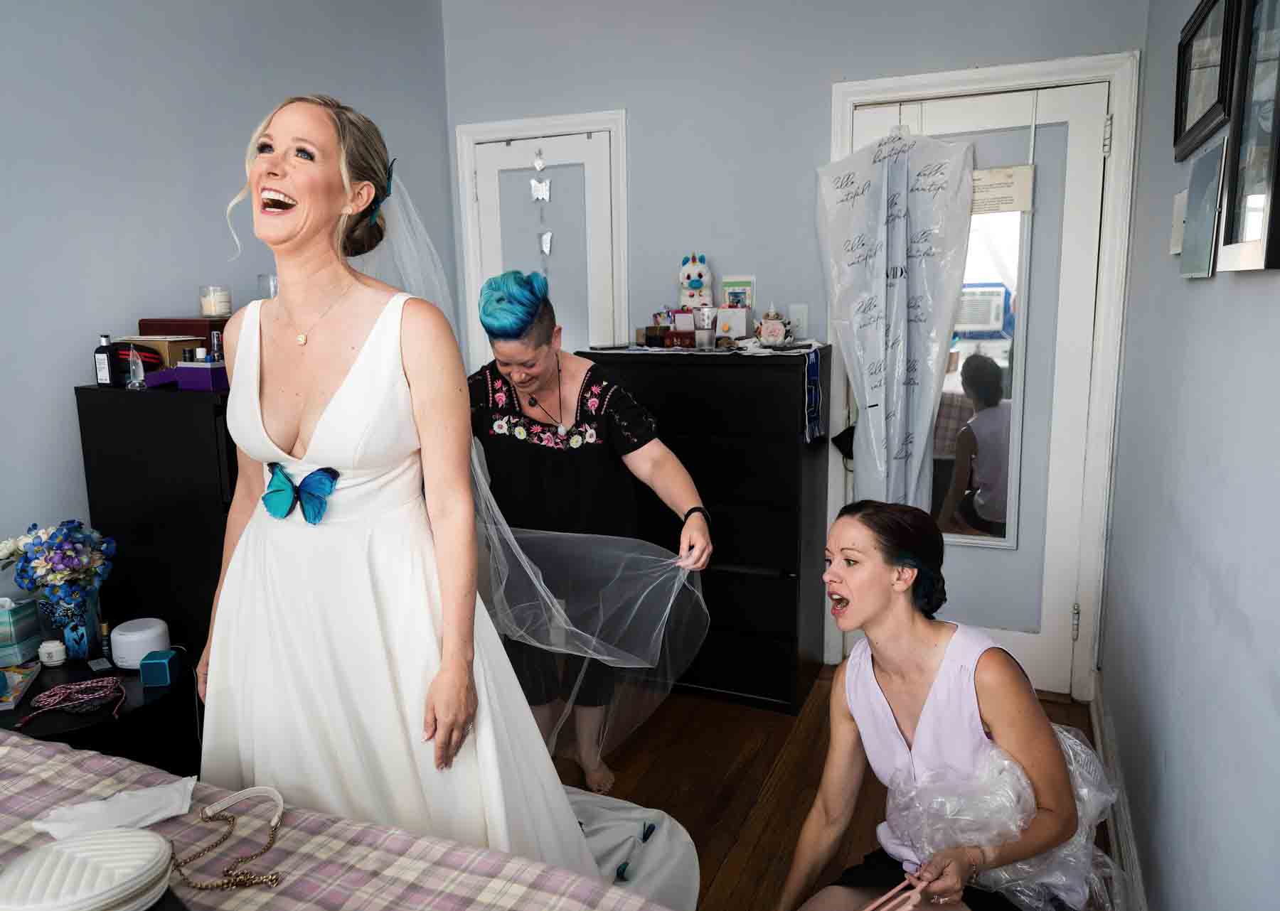 Two bridesmaids adjusting bride's veil in bedroom before wedding