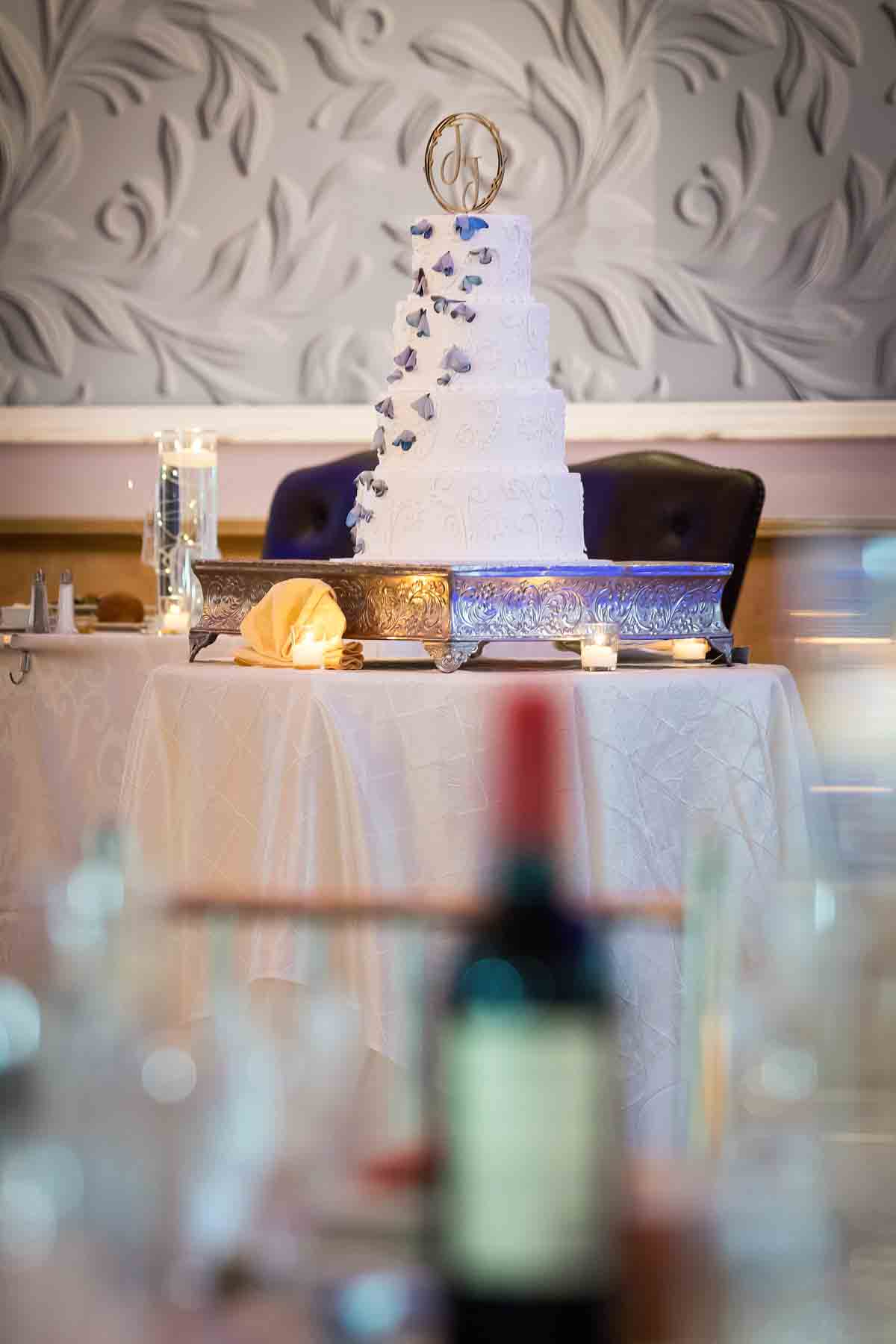 Four-layer wedding cake viewed through glasses on a table at a Terrace on the Park wedding