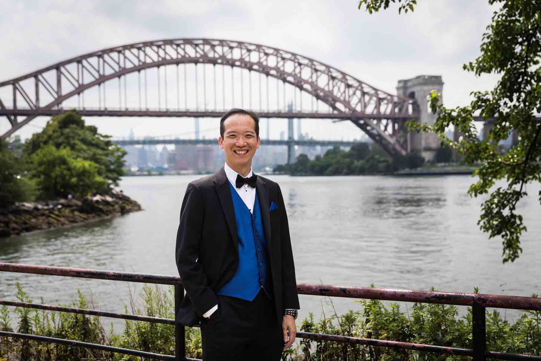 Groom wearing blue vest and tux standing along waterfront in Astoria Park