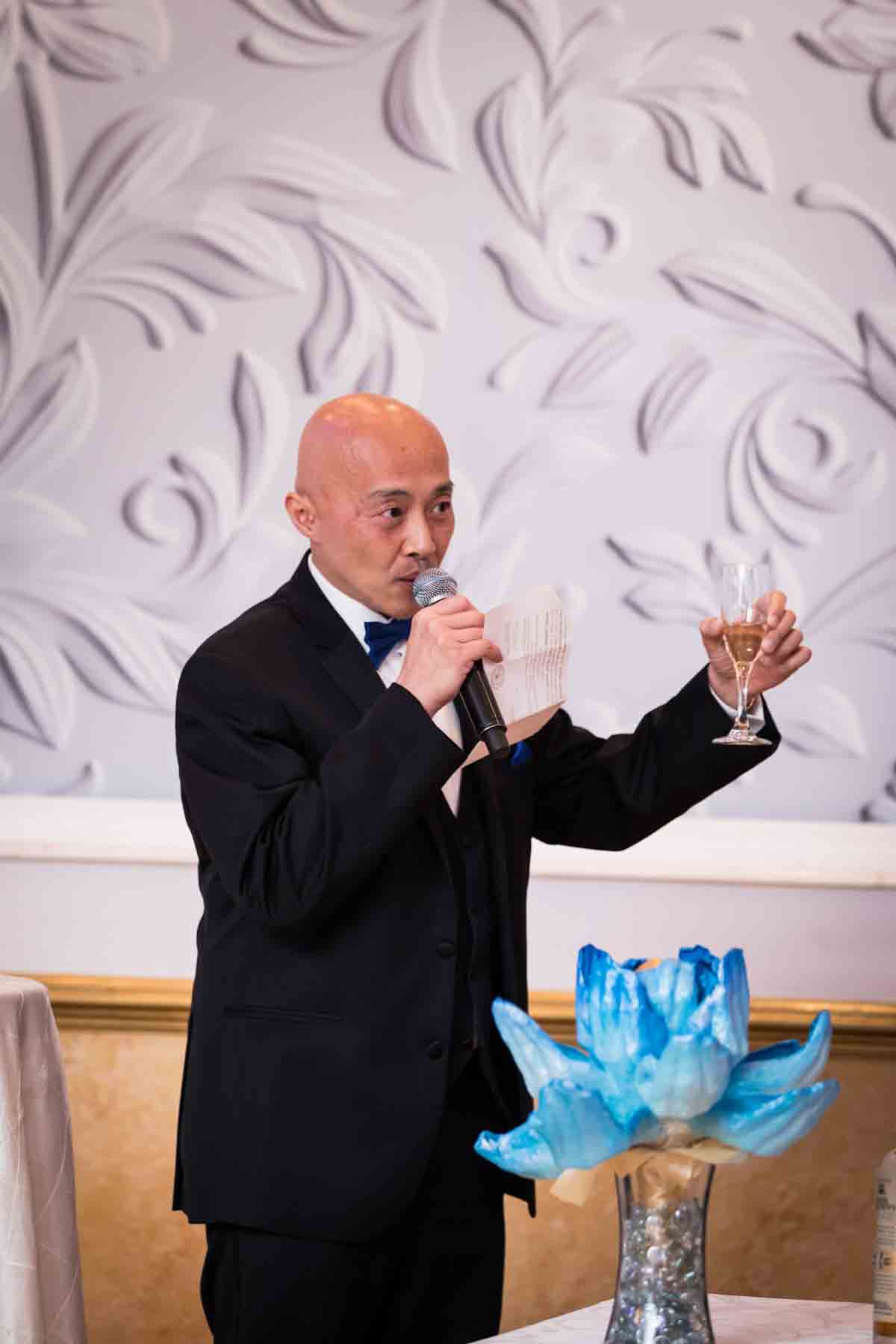 Bald Asian man raising glass of champagne while making speech at a Terrace on the Park wedding