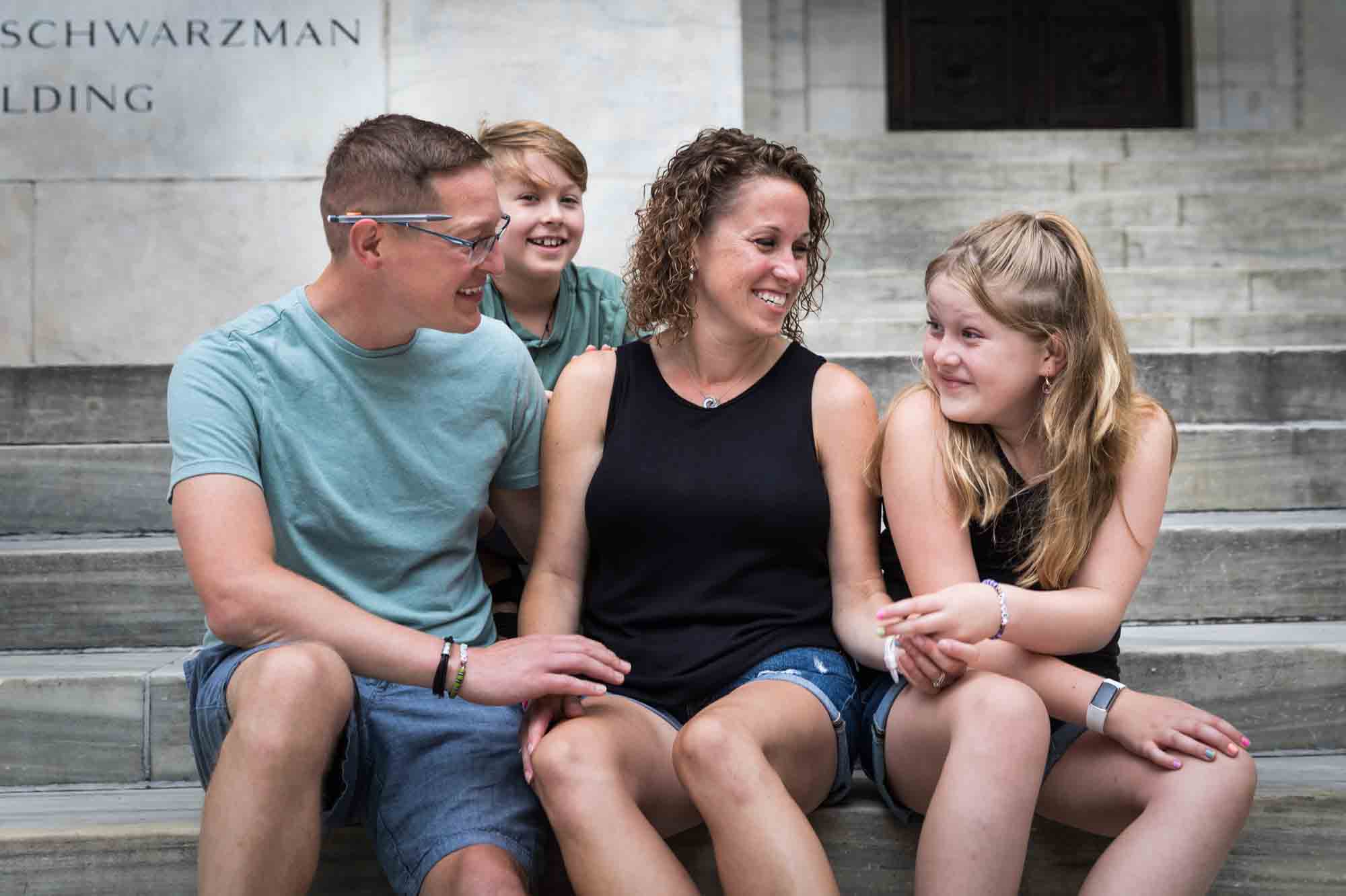 Parents and two kids sitting together on steps of New York Public Library