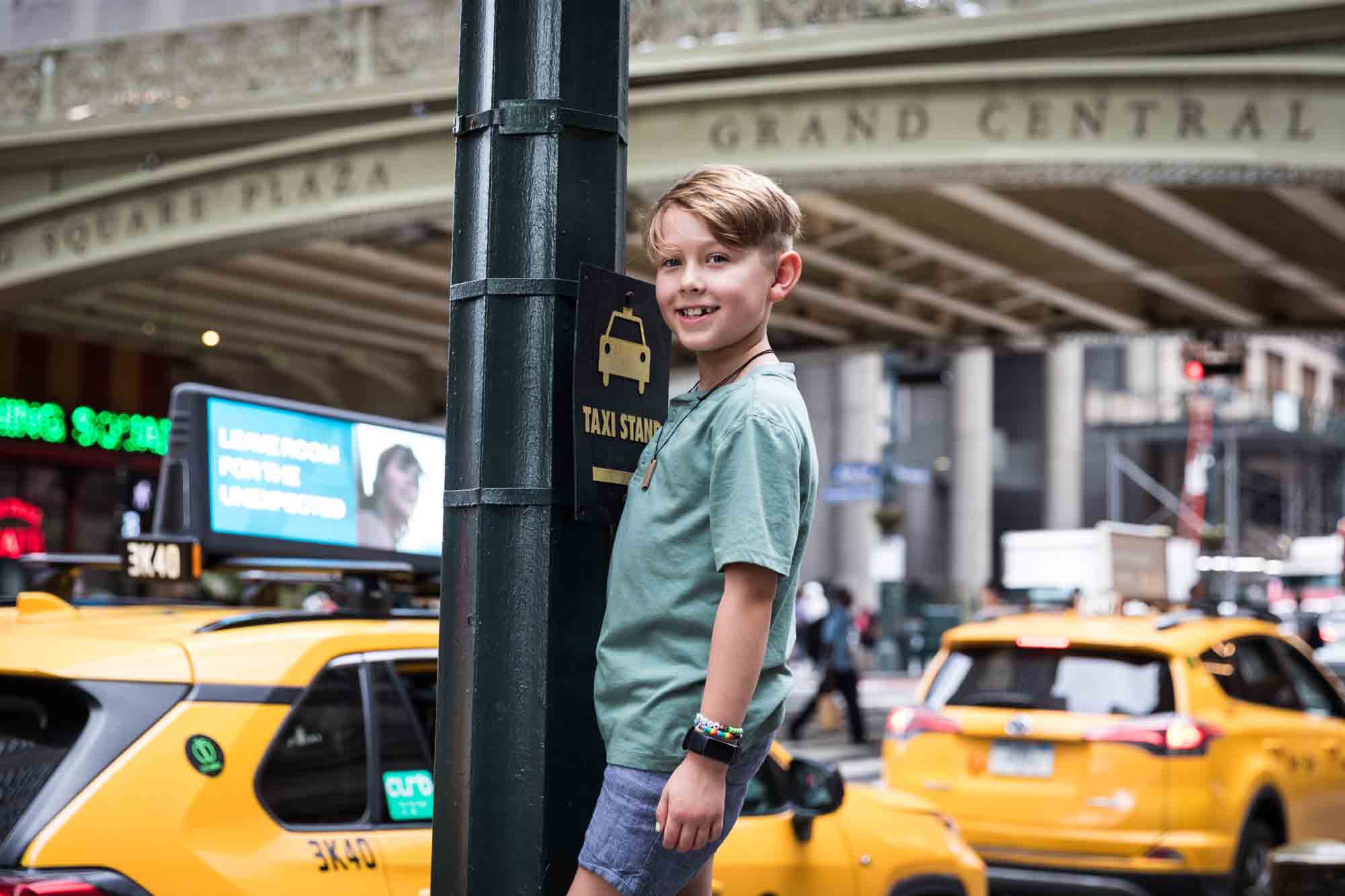 Boy standing on light pole in front of yellow taxi