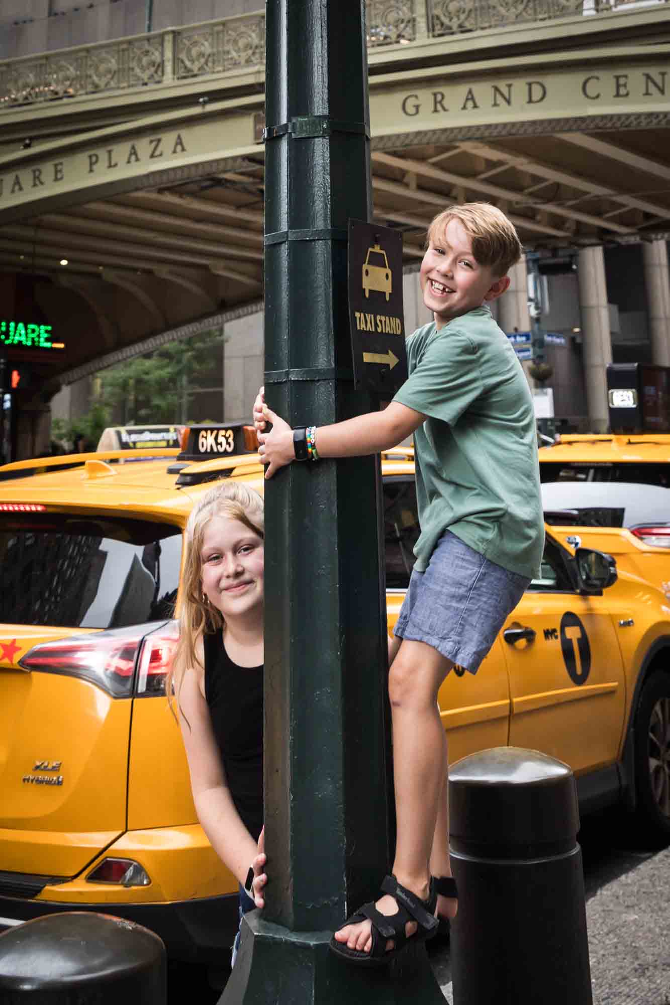 Boy and girl hugging light pole in front of yellow taxis