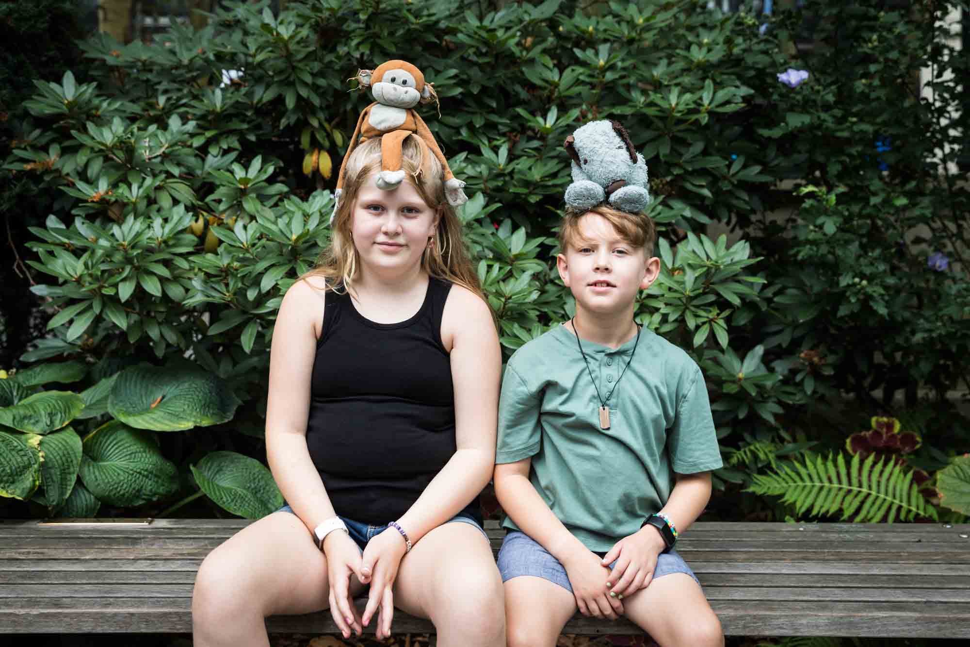 Boy and girl sitting on bench with stuffed animals on their heads