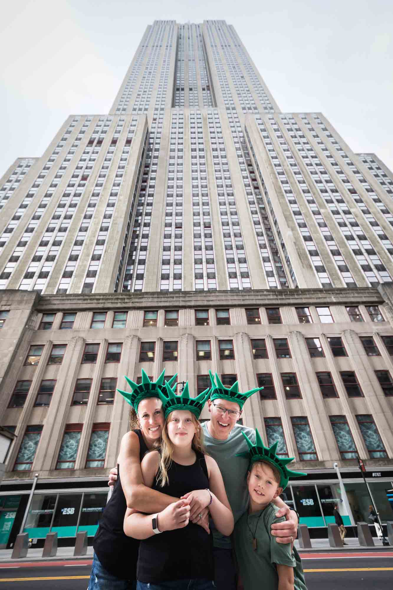 Parents and two kids with Statue of LIberty foam hats on standing in front of Empire State Building