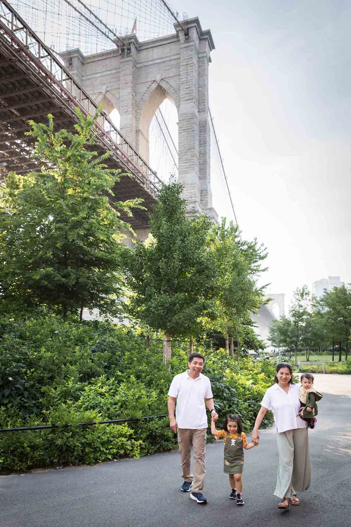 Parents walking with two daughters in front of Brooklyn Bridge for an article on Brooklyn Bridge Park family portrait tips for young children