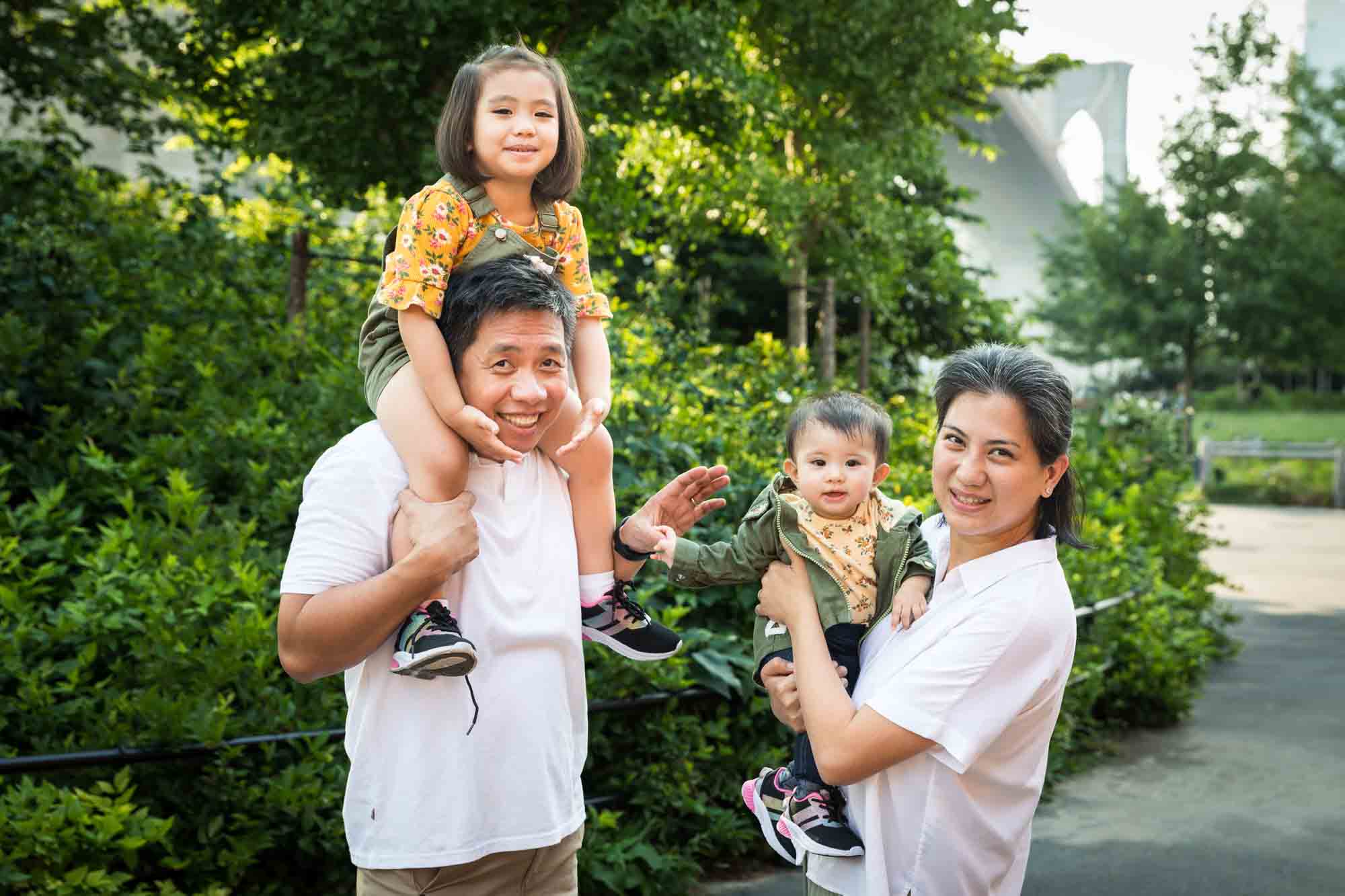 Parents holding two young children for an article on Brooklyn Bridge Park family portrait tips for young children