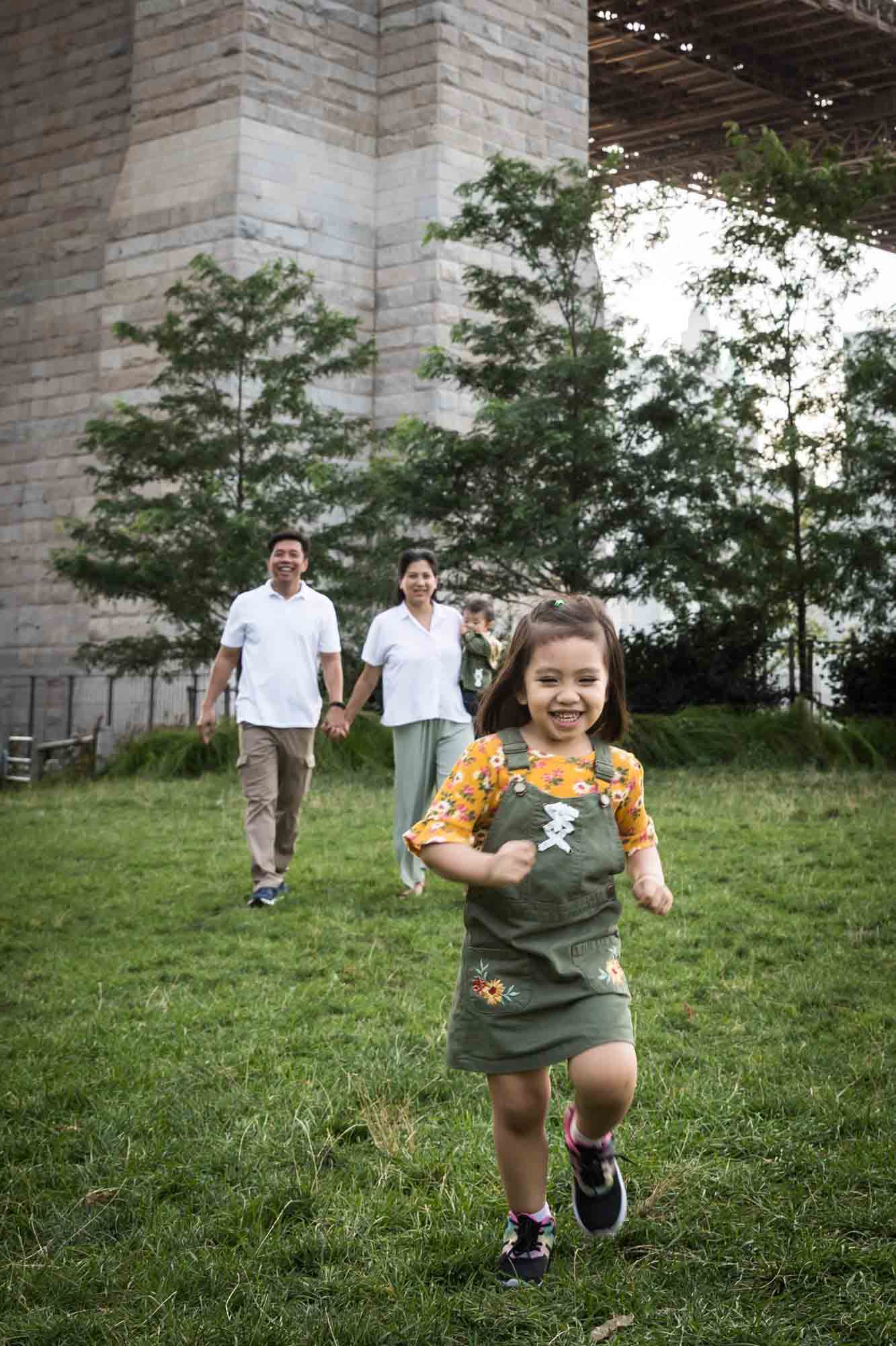 Little girl running in front of parents for an article on Brooklyn Bridge Park family portrait tips for young children