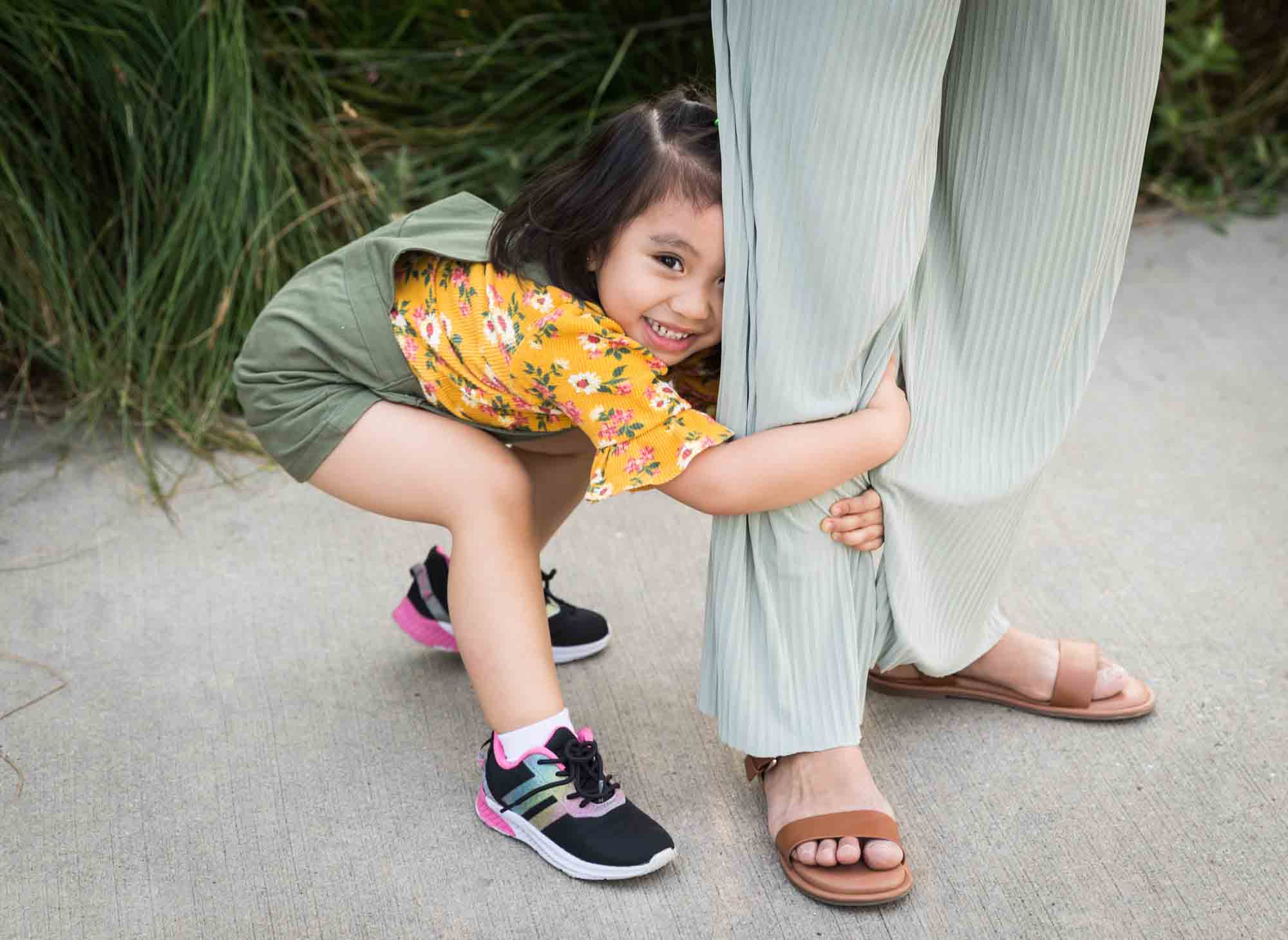 Little girl hugging mother's pant leg on the sidewalk in Brooklyn Bridge Park