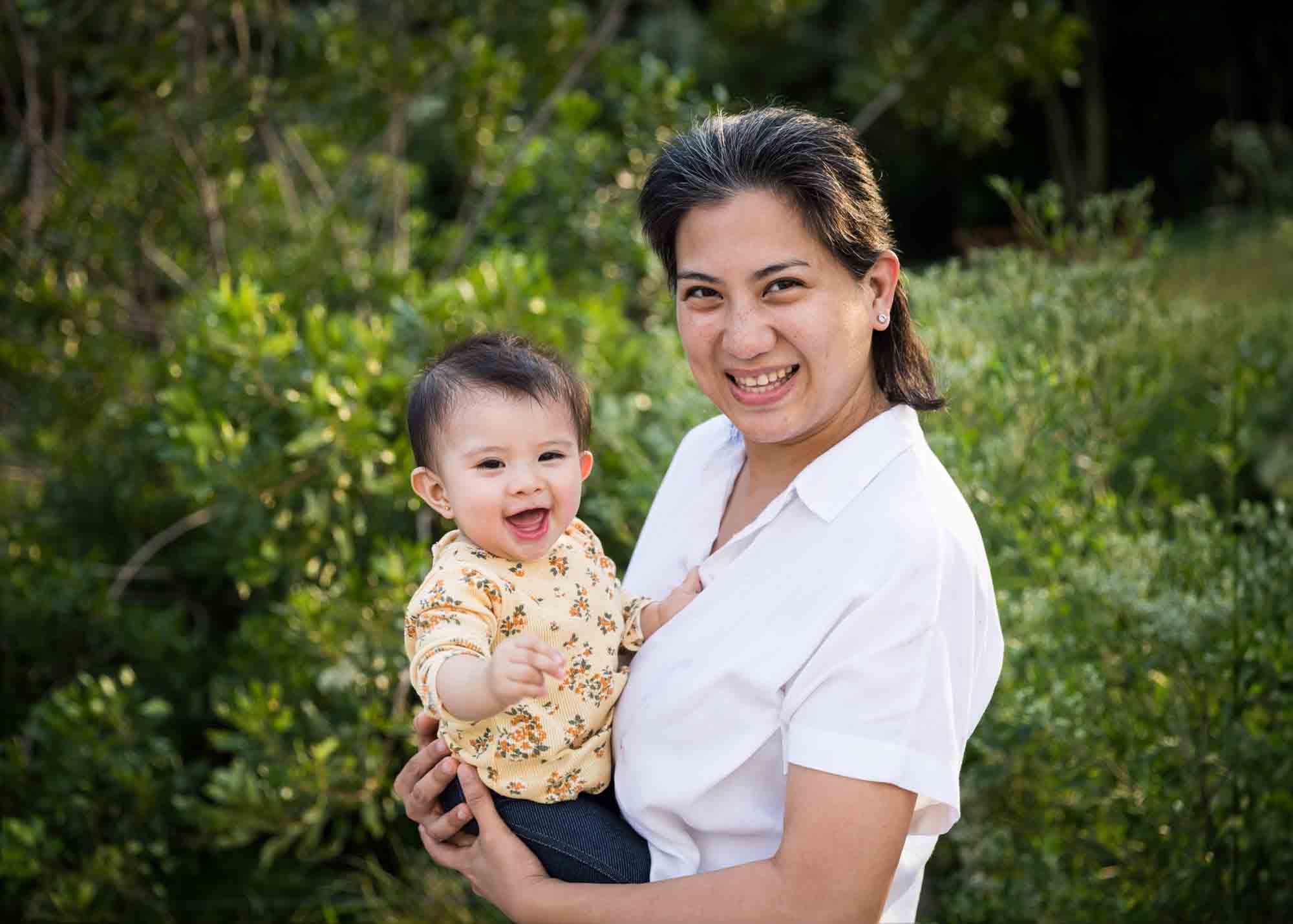 Mother holding young daughter in front of grass for an article on Brooklyn Bridge Park family portrait tips for young children