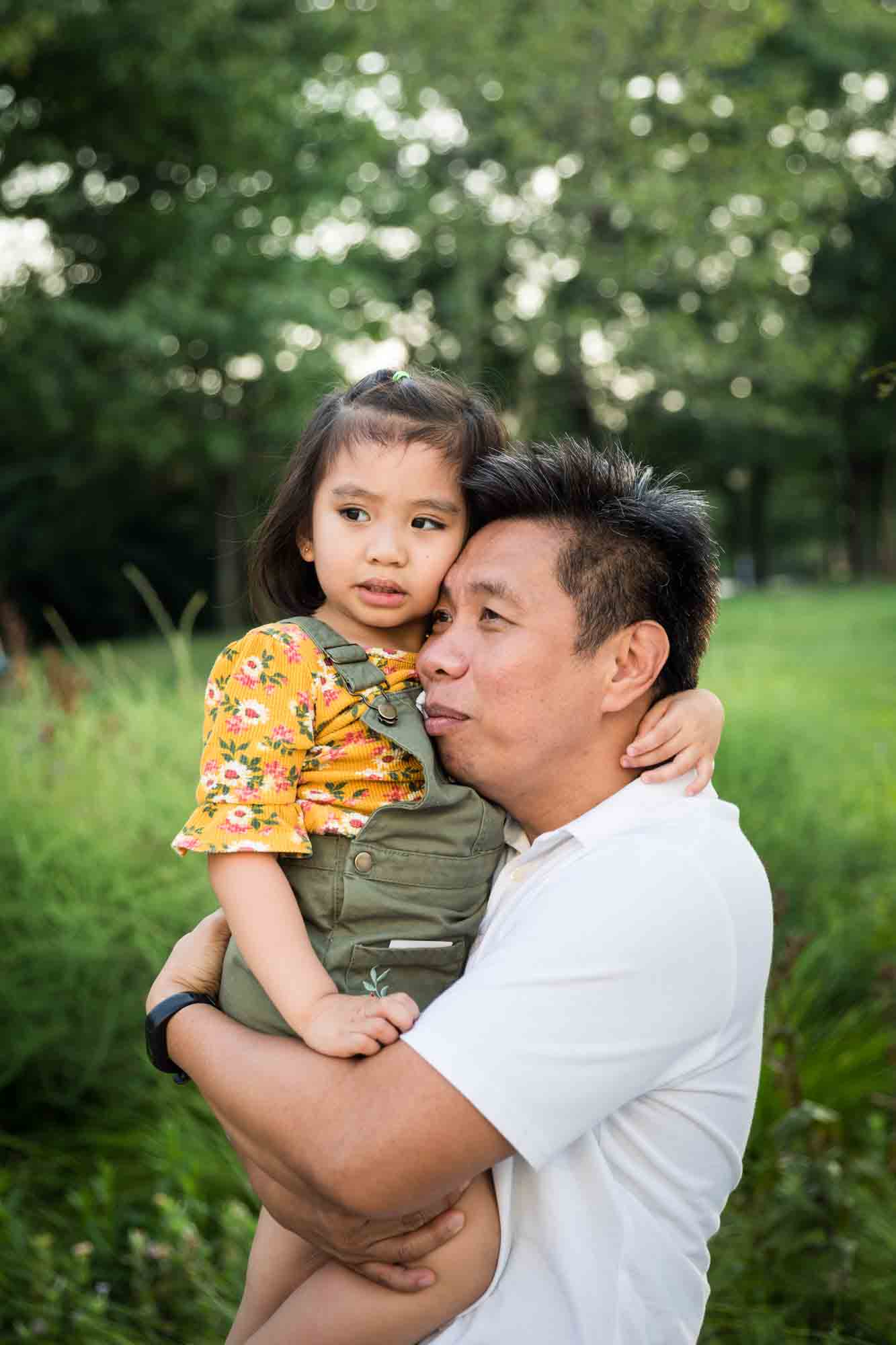 Father holding young daughter in front of grass for an article on Brooklyn Bridge Park family portrait tips for young children