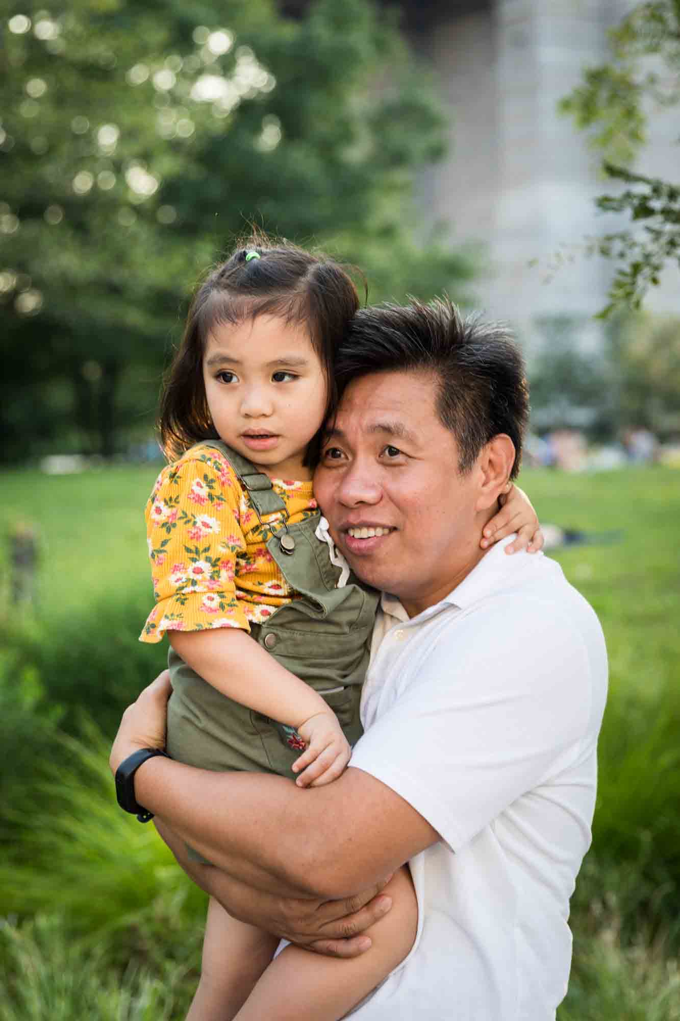 Father holding young daughter in front of grass for an article on Brooklyn Bridge Park family portrait tips for young children