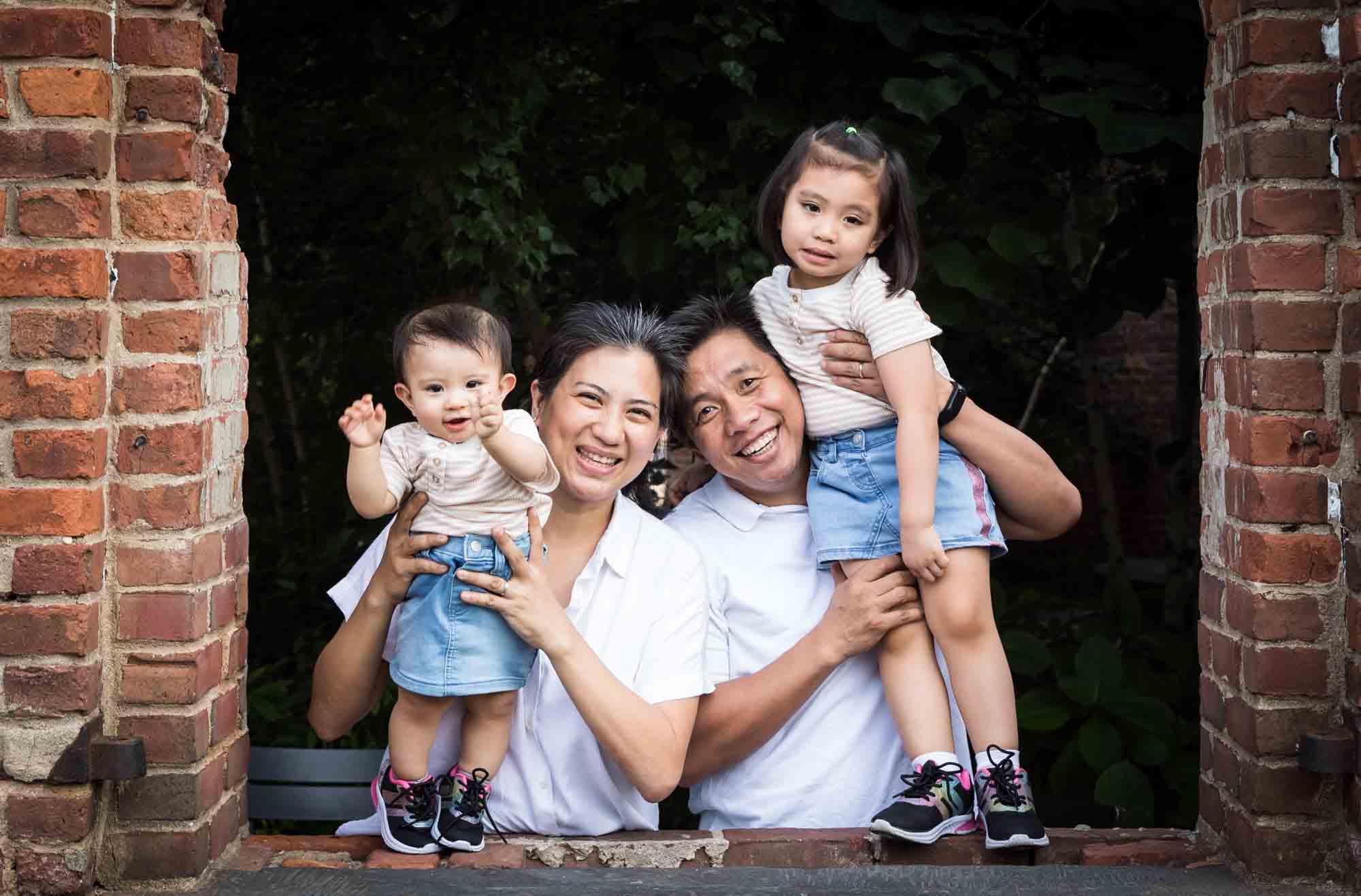 Parents holding two daughters in brick windowsill for an article on Brooklyn Bridge Park family portrait tips for young children