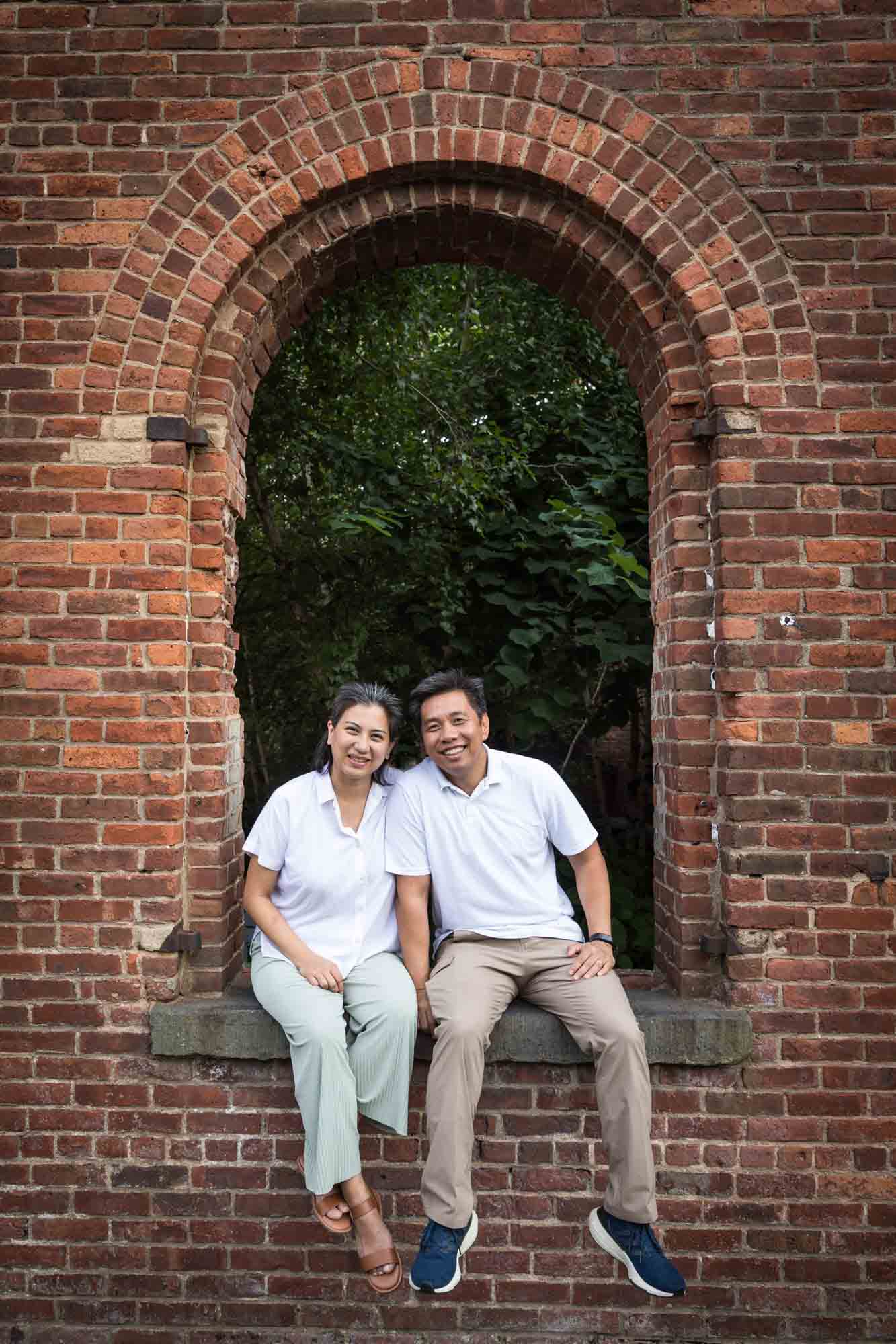 Couple sitting together in brick window of Max's Family Garden for an article on Brooklyn Bridge Park family portrait tips for young children