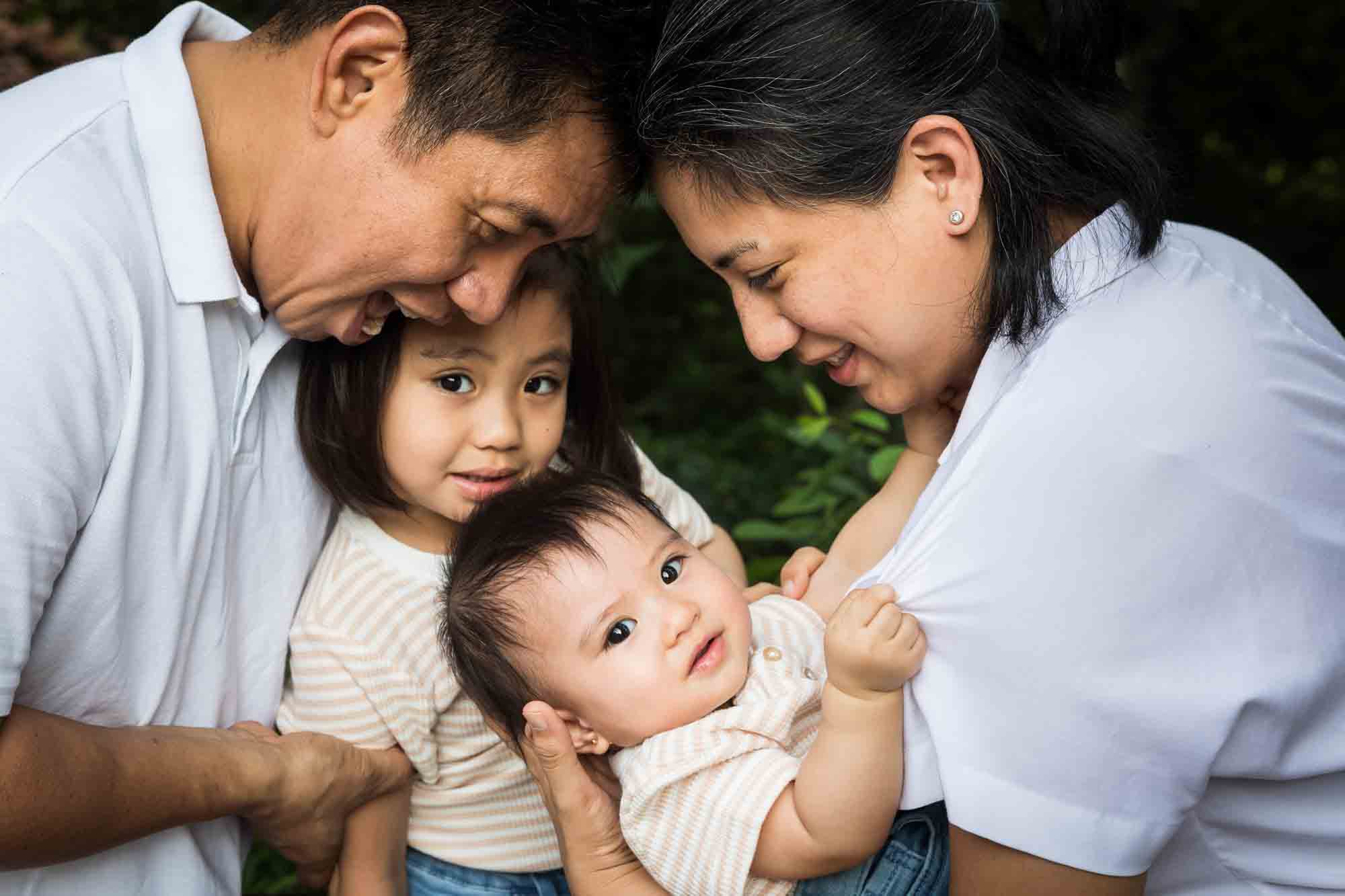 Parents holding baby girl in front of older sister for an article on Brooklyn Bridge Park family portrait tips for young children