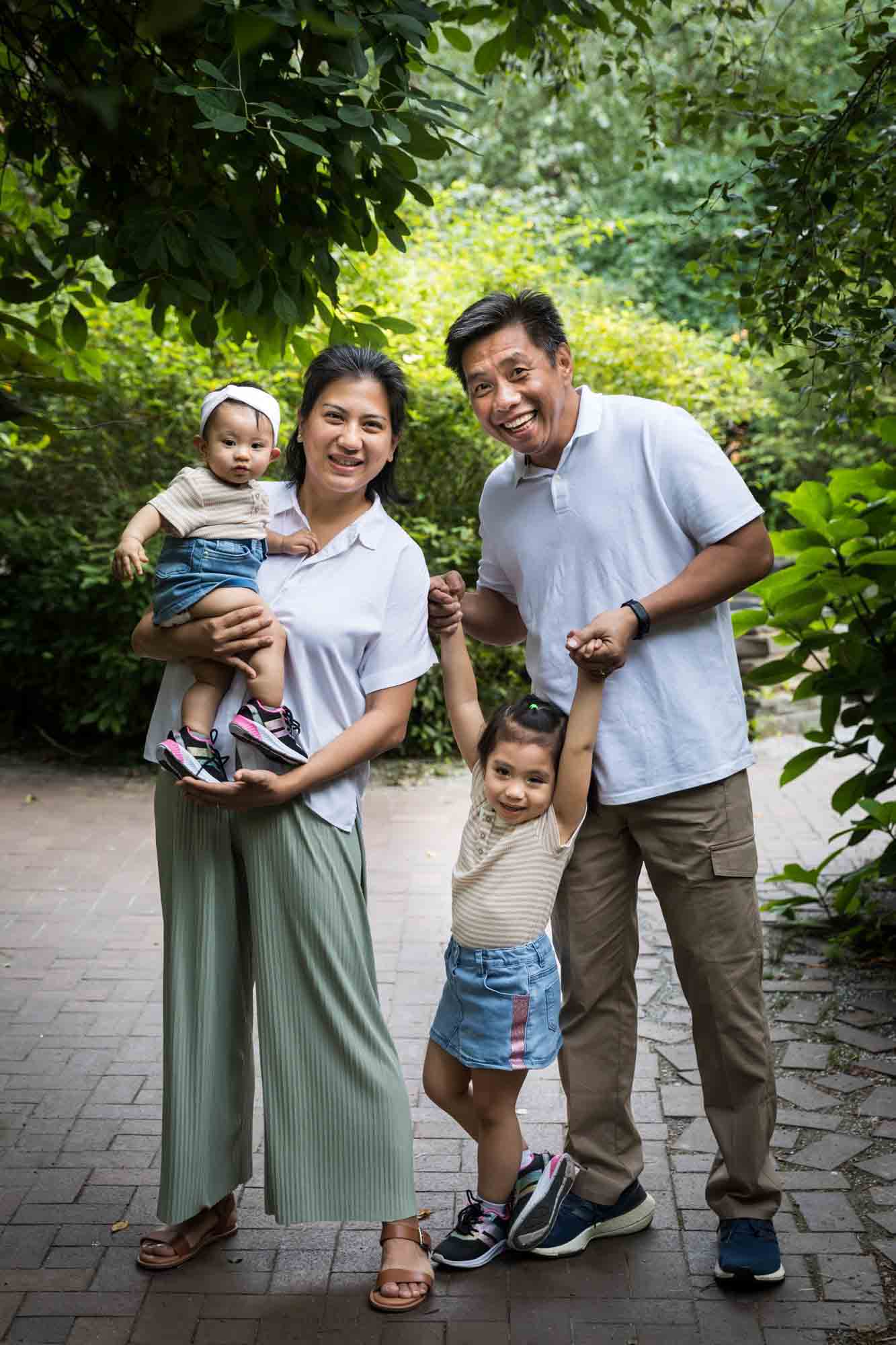 Parents standing with two daughters in front of trees for an article on Brooklyn Bridge Park family portrait tips for young children