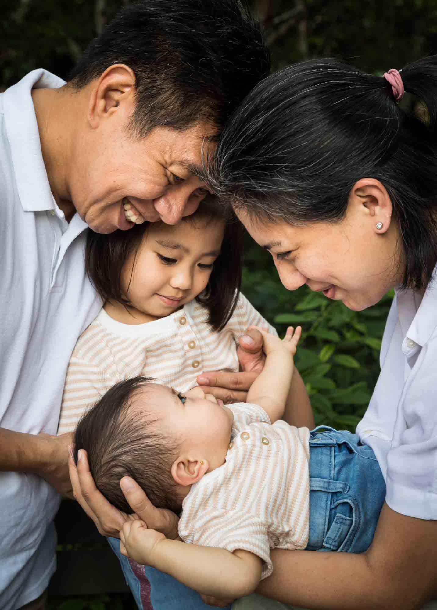 Parents holding baby girl in front of older sister for an article on Brooklyn Bridge Park family portrait tips for young children